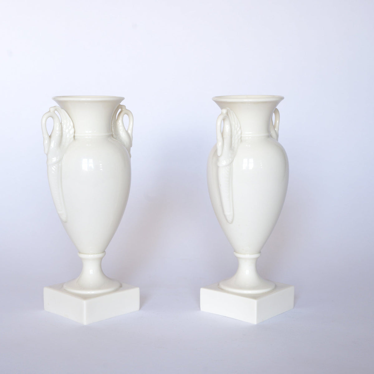 Pair of Euro Trash Vintage White Swan Handle Ceramic Urn Vases, each on a square base and designed as classic pedestal vases, displayed against a white background.