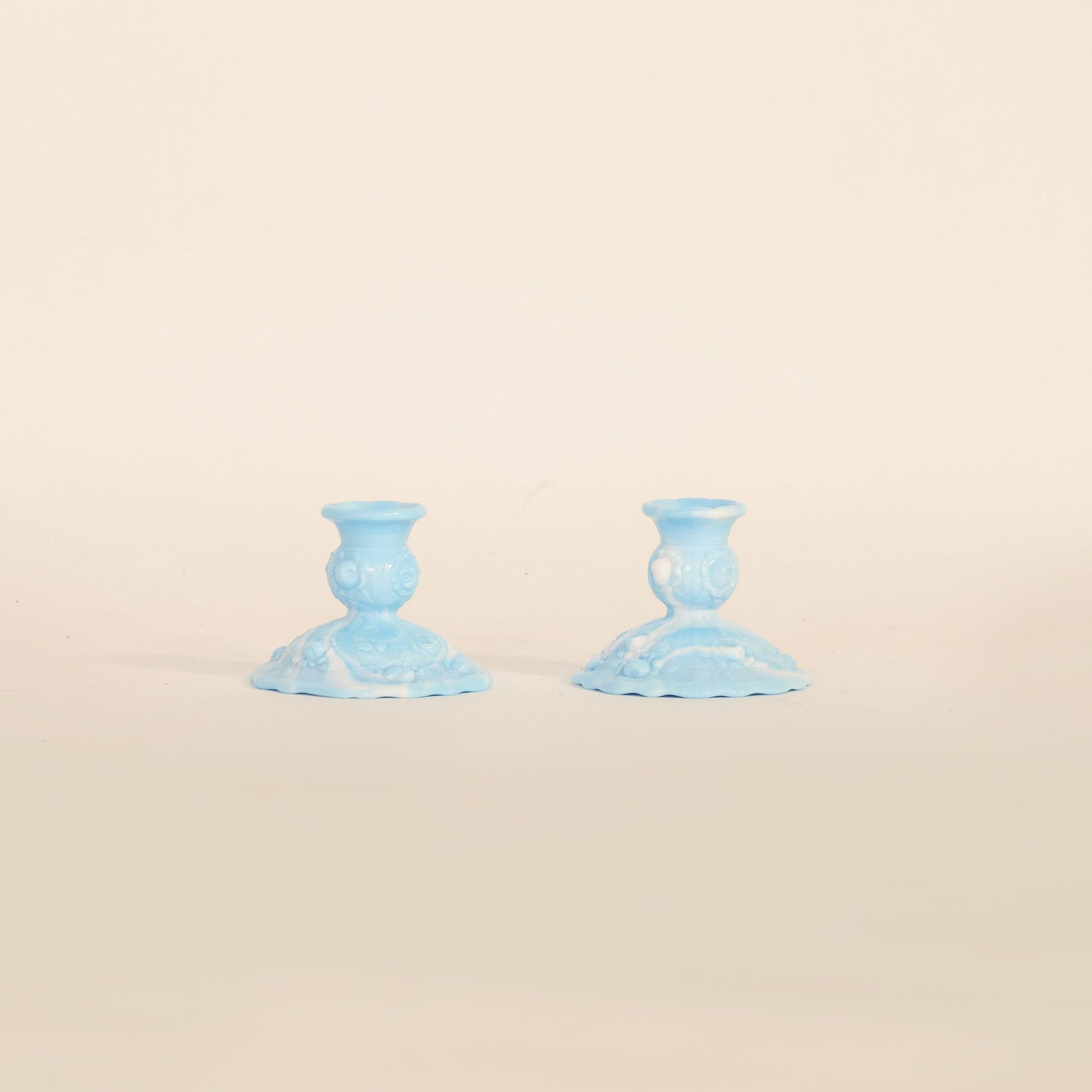 The Vintage Pair Of Blue Milk Glass Candlestick Holders by Euro Trash Annie, featuring a delicate pressed pattern, are displayed side by side on a plain beige background.