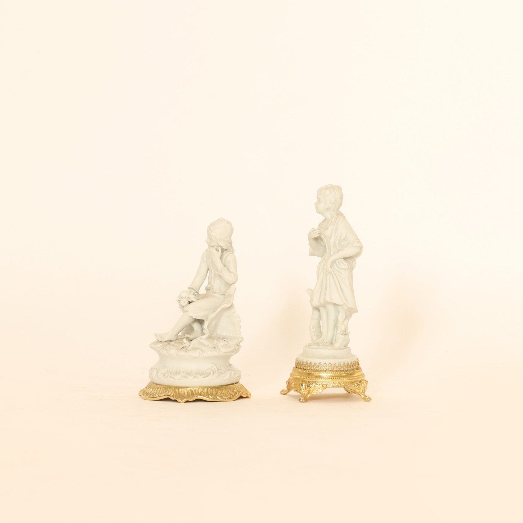 Two statue figurines on gold bases against a beige background