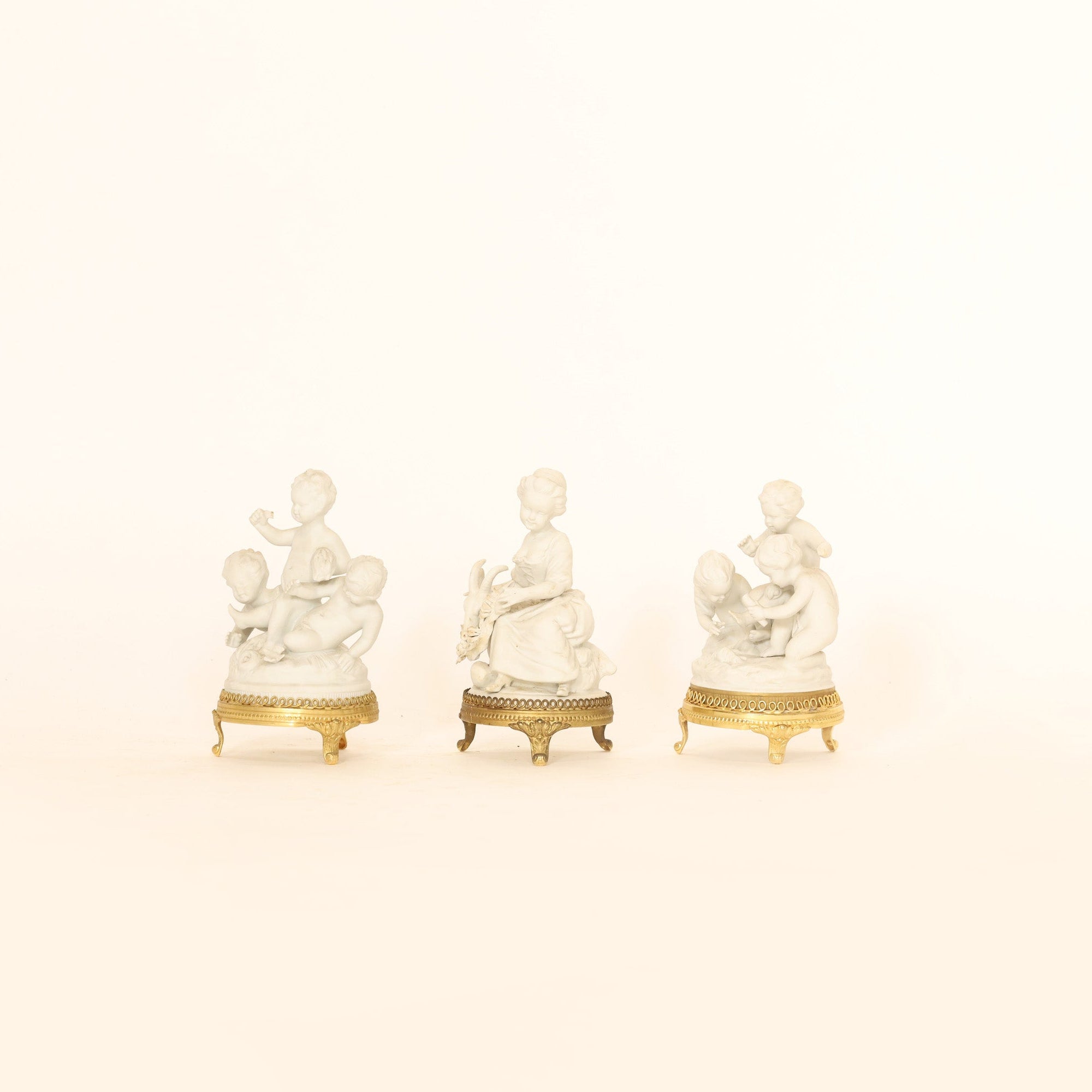 Three white figurines with gold bases on a beige background