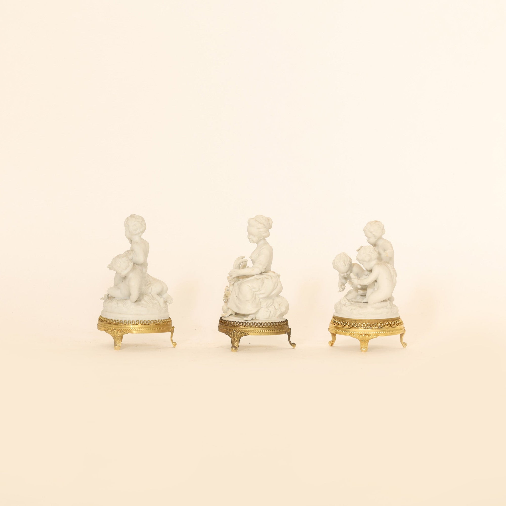 Three white figurines with gold bases on a beige background