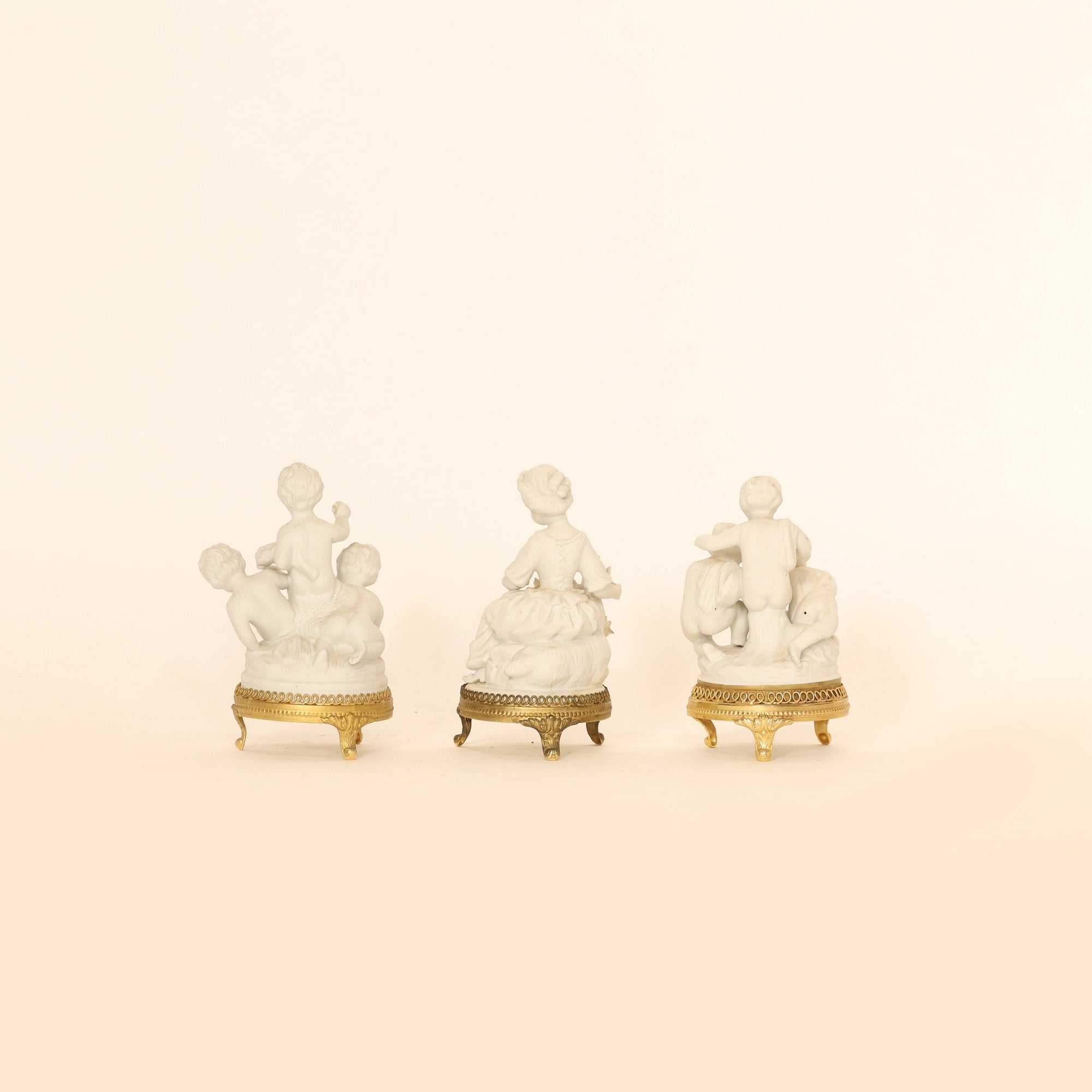 Three white figures with gold bases on a beige background