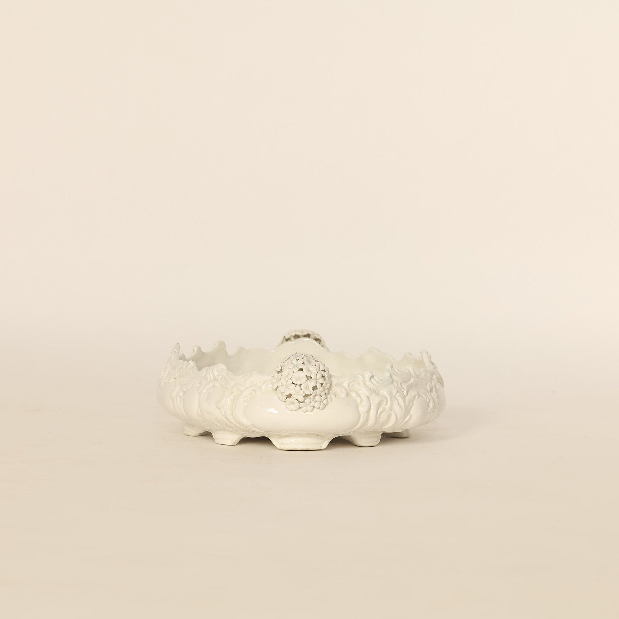 Decorative white ceramic pot with intricate designs on a beige background