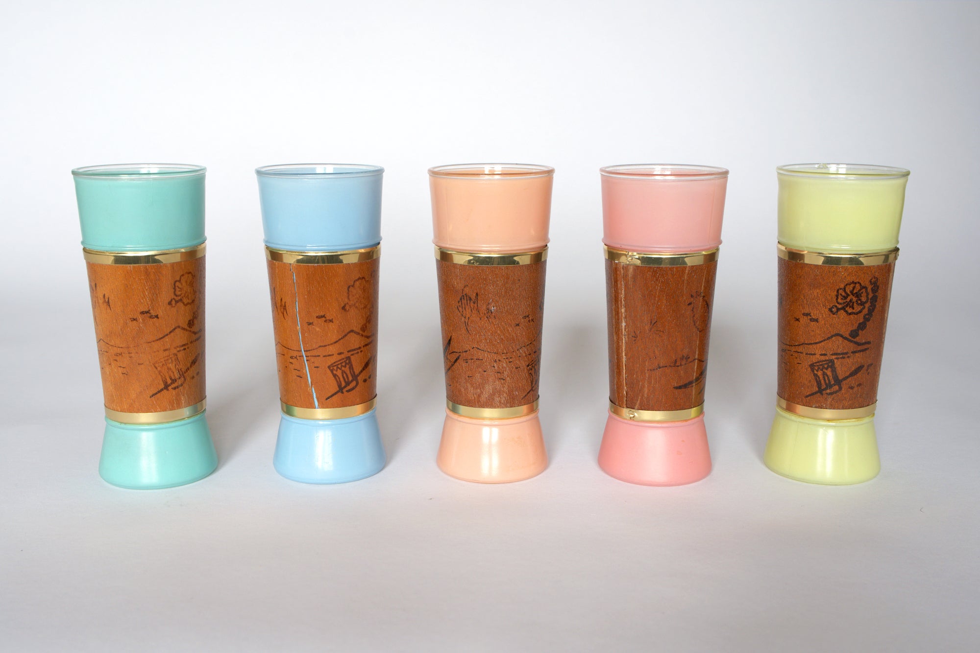 Set of five Euro Trash Mid-Century Modern Patio Glasses with pastel bases and tops (mint, blue, peach, pink, yellow), each wrapped in brown leather engraved with gold trim—ideal retro barware for décor lovers.