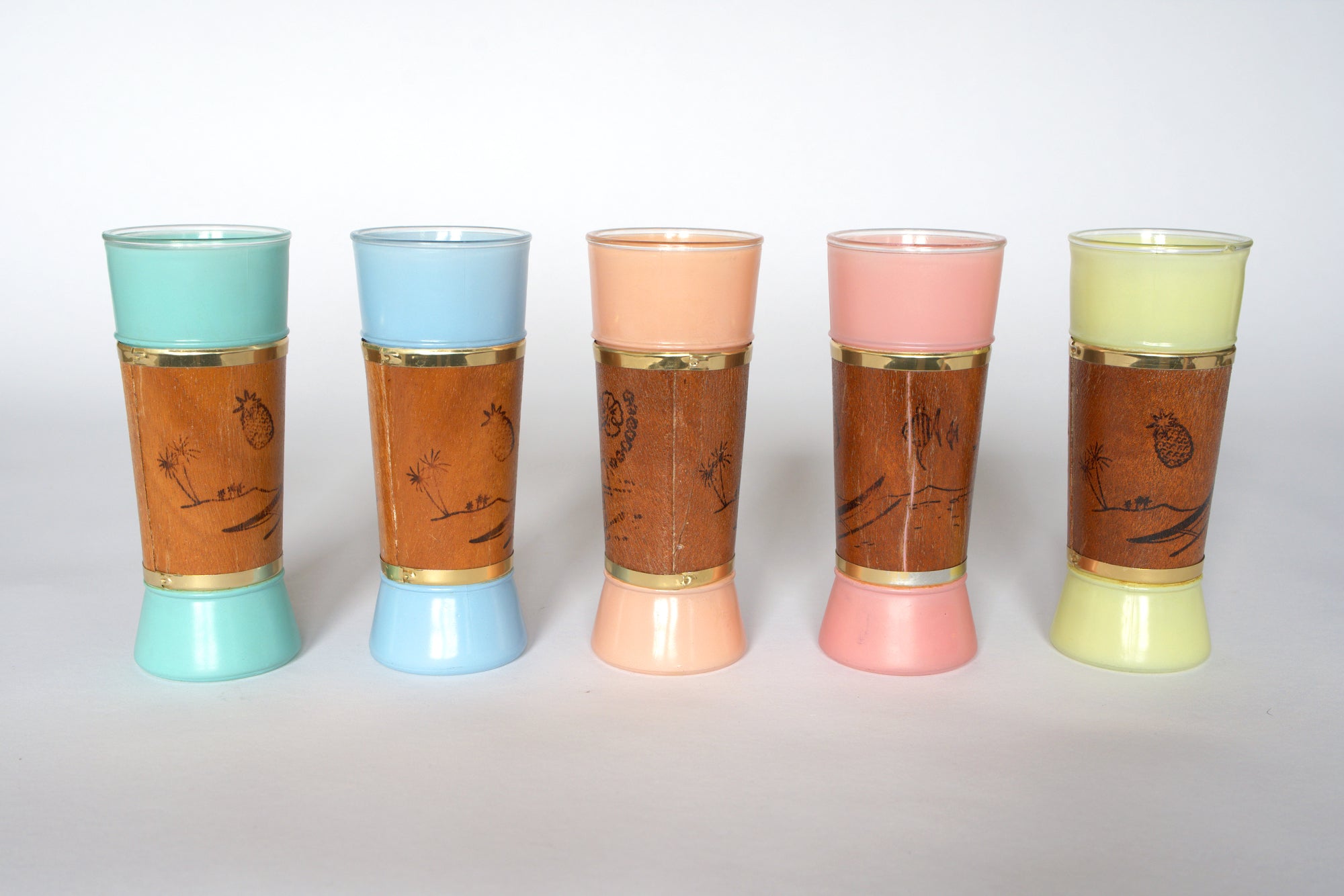 Set of five Euro Trash Mid-Century Modern Patio Glasses with pastel-colored bases and tops (aqua, blue, peach, pink, yellow), brown center with gold rim, and etched tropical designs—ideal retro décor for your barware collection.
