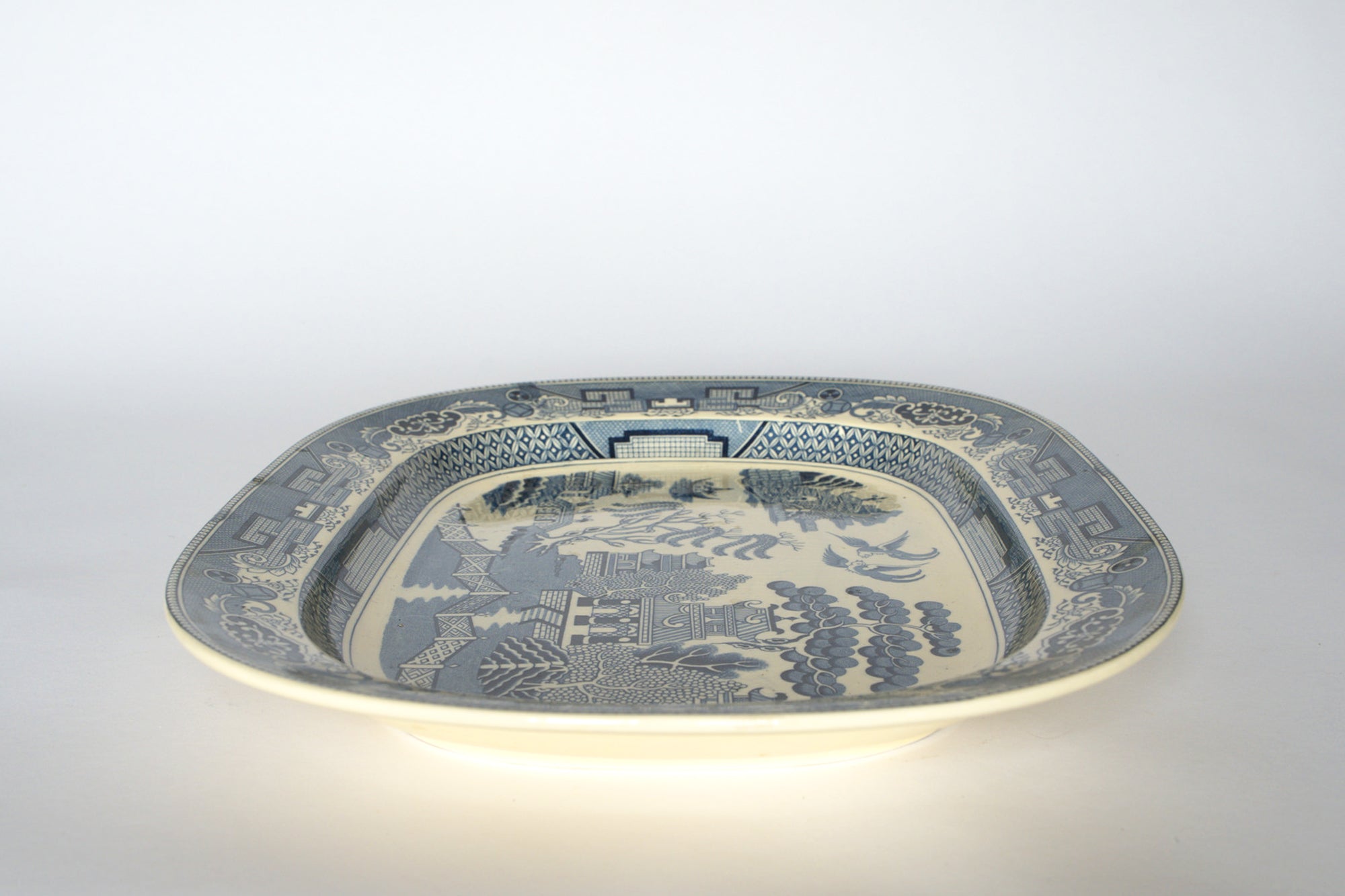 The Euro Trash Vintage Blue Willow Oval Serving Platter showcases a classic cobalt blue oriental landscape with pagodas, trees, and scenery on a crisp white background.