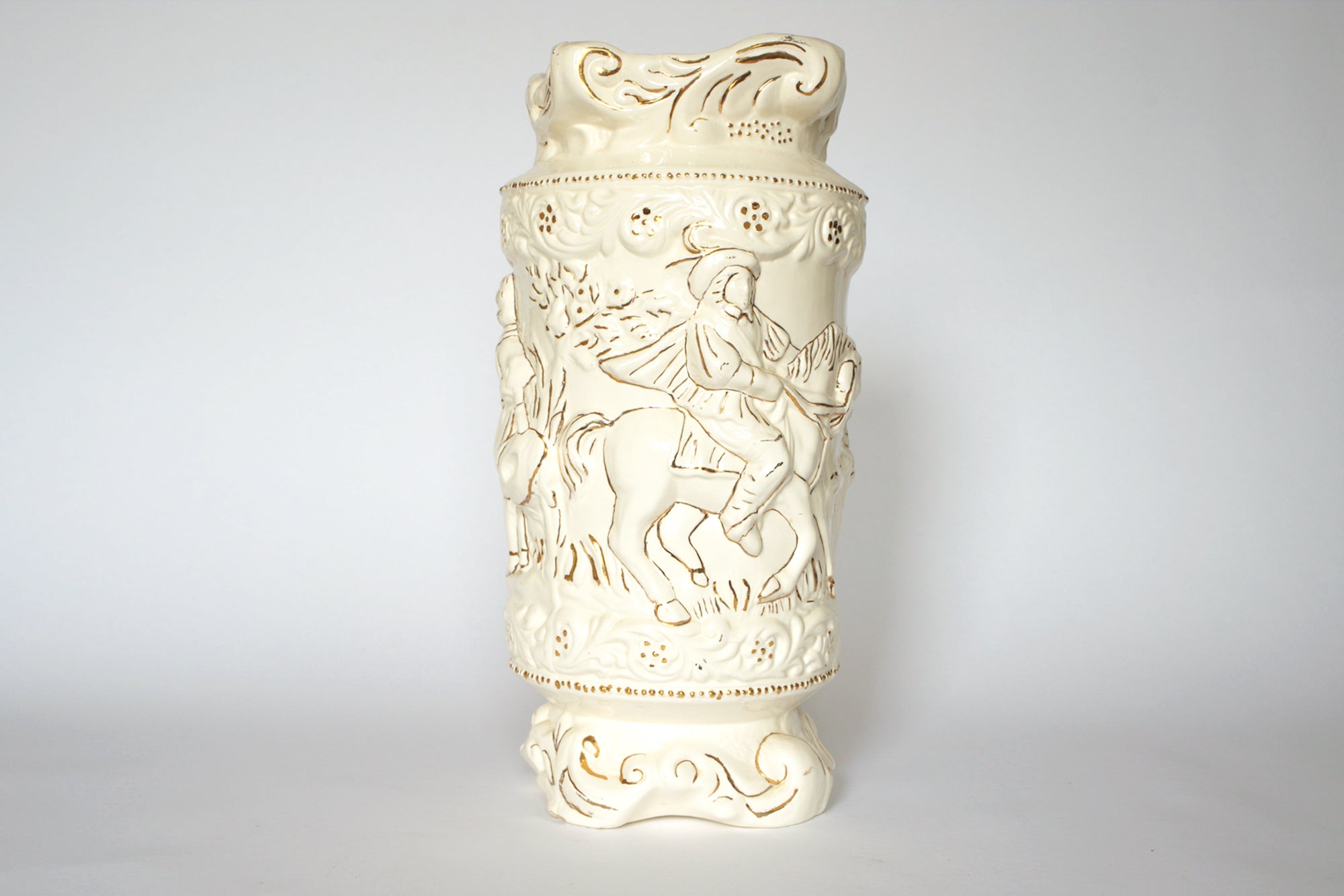 The Euro Trash Vintage Figural Porcelain Vase is a cream-colored, ornate piece featuring embossed decorative patterns and a scene of a person riding a horse, displayed against a plain white background.