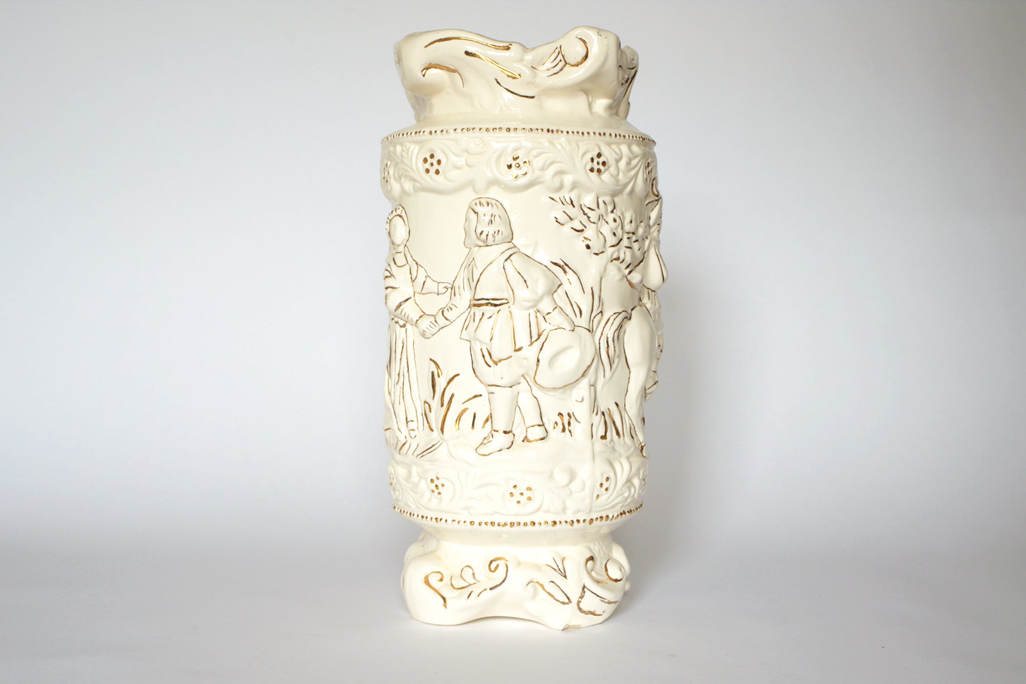 The Euro Trash Vintage Figural Porcelain Vase features cream-toned porcelain with ornate raised carvings of figures in traditional attire, foliage, and floral patterns, set against a plain white background.