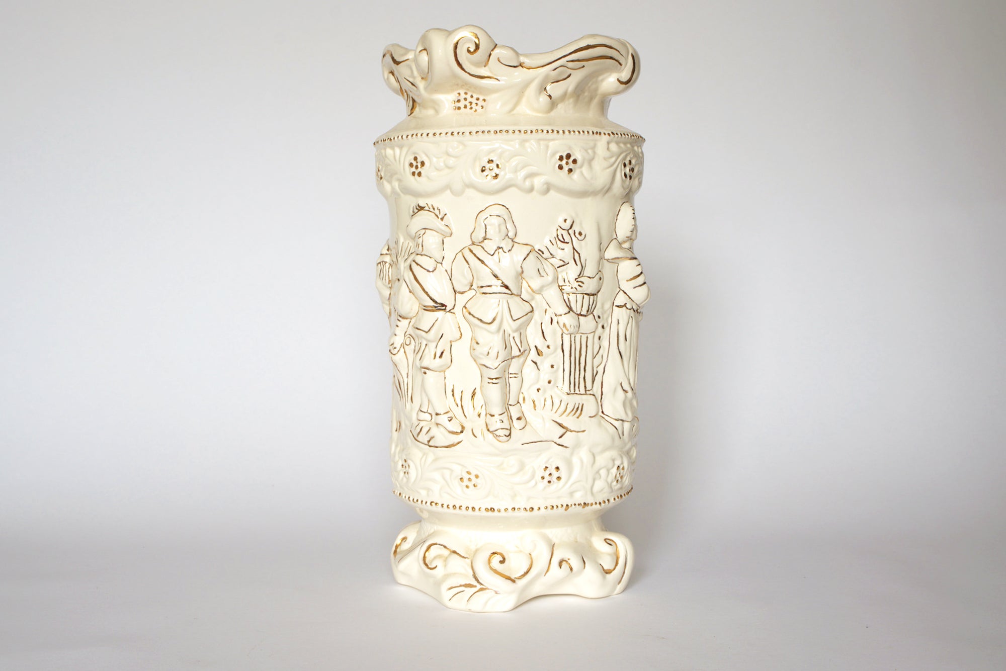 The Euro Trash Vintage Figural Porcelain Vase features an ivory finish with embossed scenes of standing figures in historical attire, surrounded by decorative floral and scroll patterns, set against a plain white background.