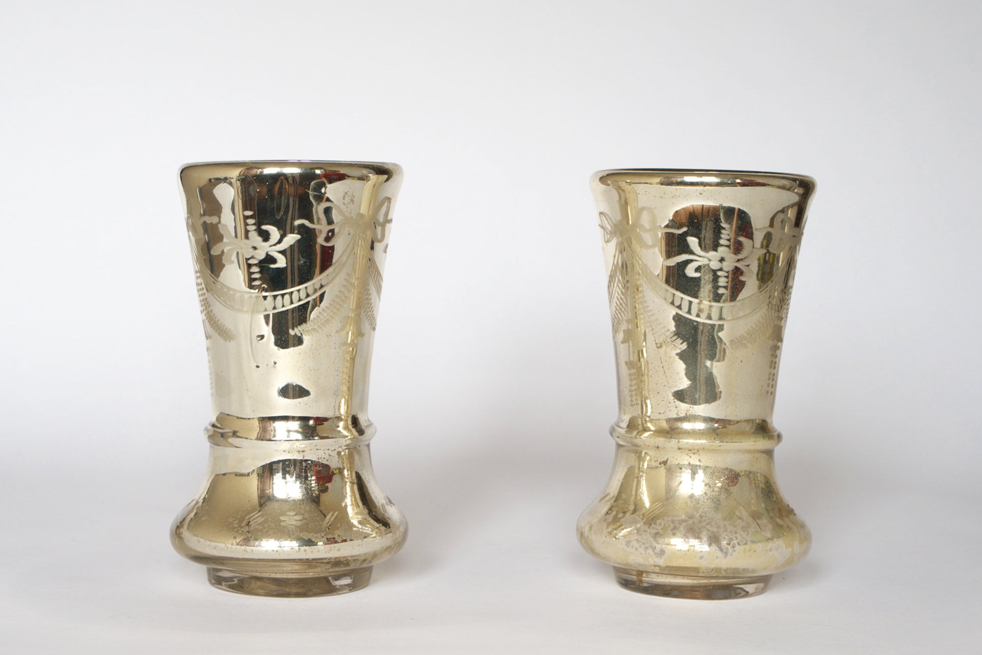 The Pair of Vintage Etched Mercury Glass Vases by Euro Trash features flared tops, engraved patterns, a silvered reflective finish, and rounded bases, showcased against a plain white background.