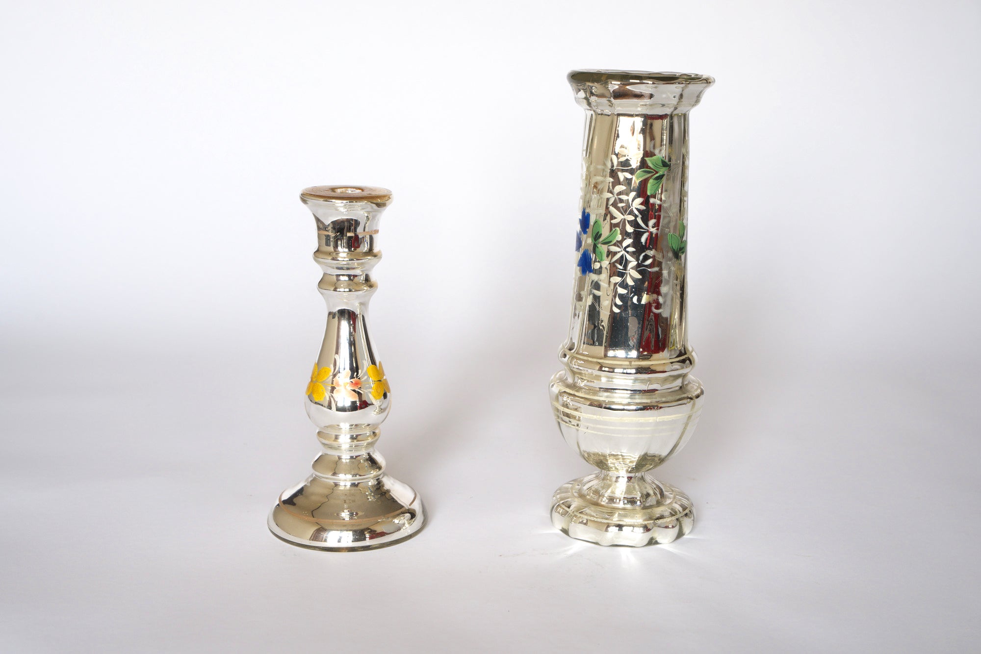 Set of two silver mercury glass vases by Euro Trash on a white background: one short with hand-painted floral details, and one taller, both featuring colorful vintage-inspired floral patterns.
