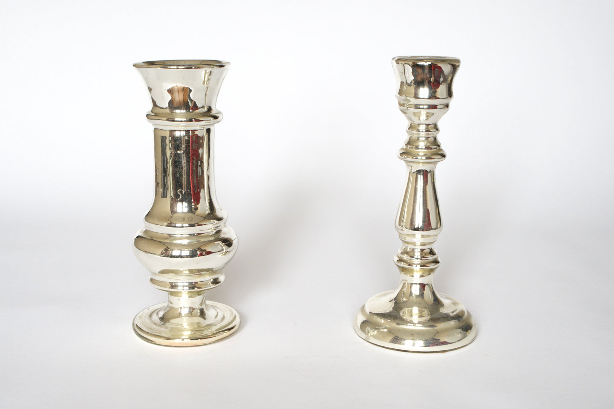 A pair of Euro Trash Vintage Mercury Glass Candleholders, each with a unique design, stand upright on a plain white background.