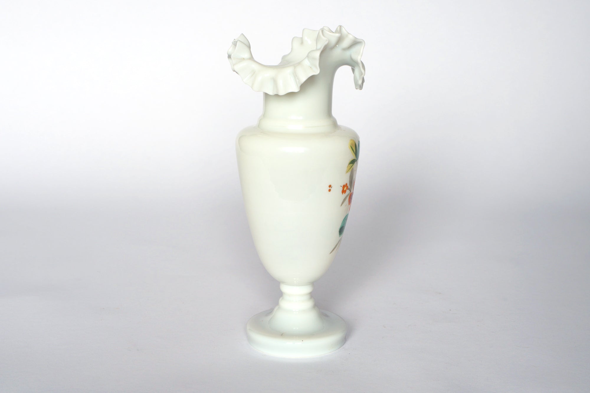 The Euro Trash Vintage Hand-Painted Milk Glass Vase features a narrow stem, wide body, ruffled rim, and one side adorned with floral designs. Displayed against a white background.
