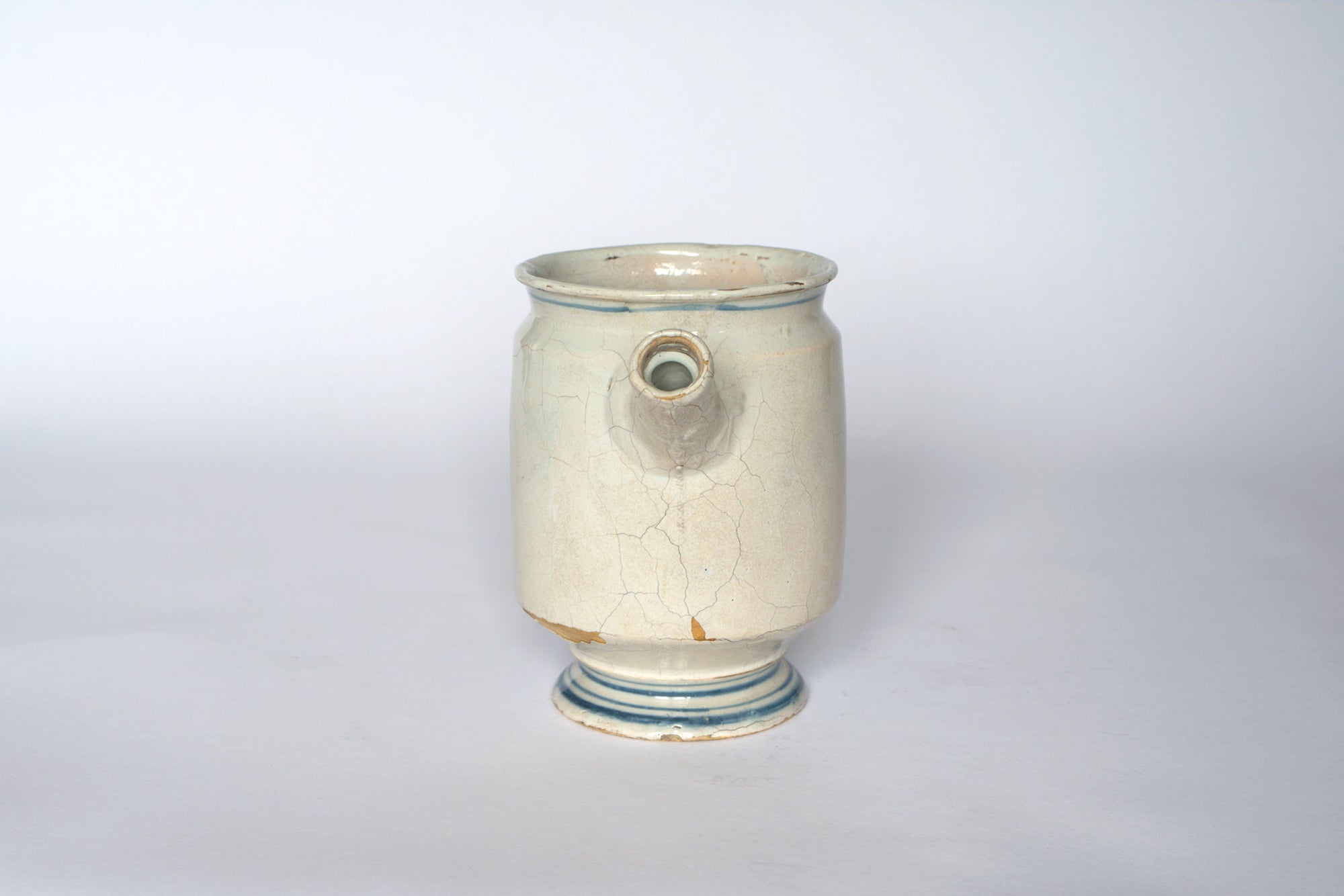 The Euro Trash Vintage Hand-Painted Blue & Cream Ceramic Pitcher features a wide circular base, small spout, blue detailing, and visible cracks, displayed against a plain white background.