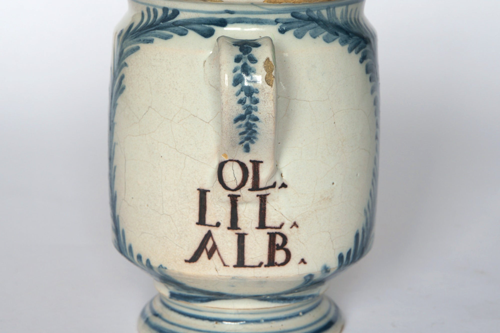 A close-up of the Euro Trash Vintage Hand-Painted Blue & Cream Ceramic Pitcher, featuring leafy blue patterns, a handle, "OL. LIL. ALB." in brown, and fine surface crack lines for an authentic vintage look.