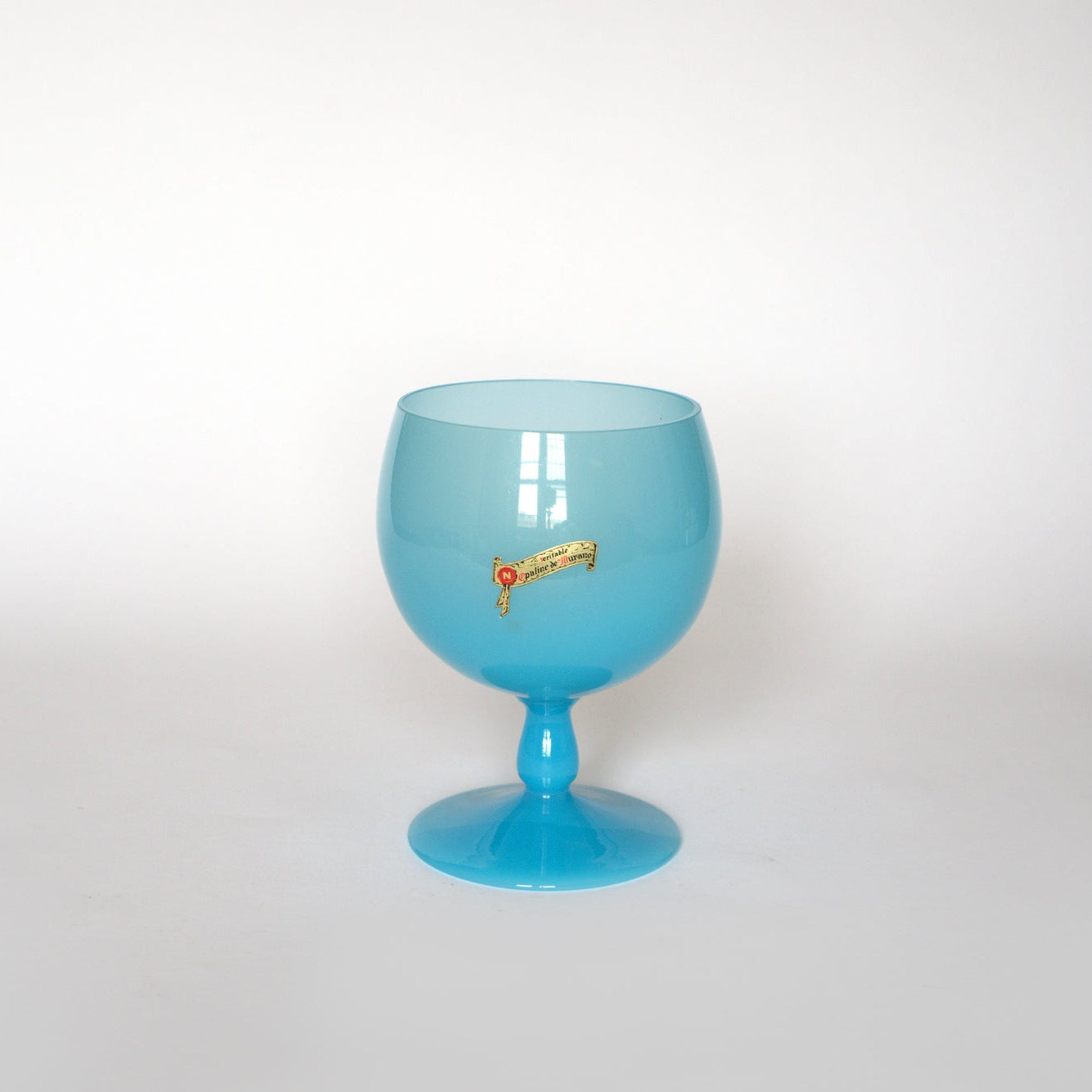 The Euro Trash Vintage Blue Opaline Murano Glass Goblet features a large, round design with a short stem and gold and red emblem, displayed on a white surface with a plain white background—a standout collectible art glass piece.