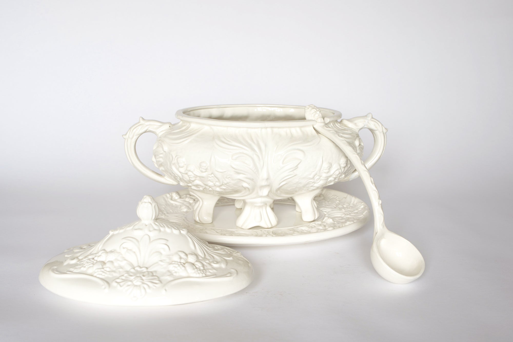 The Euro Trash Vintage White Ceramic Tureen with Underplate and Ladle features ornate floral and leaf patterns, two handles, a matching lid, and comes as an elegant decorative soup serving set.