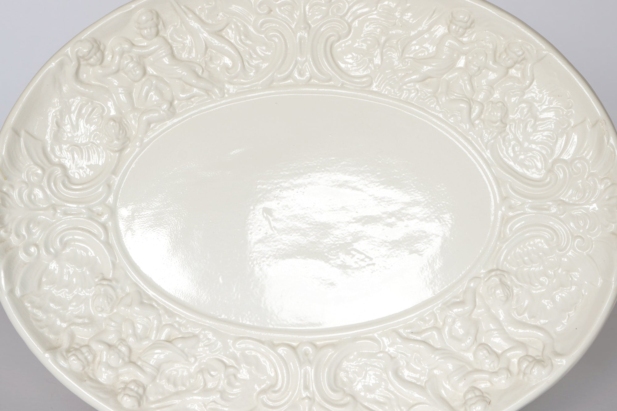 The Euro Trash Vintage White Ceramic Tureen with Underplate and Ladle features an oval white ceramic plate adorned with intricate embossed rim designs reminiscent of classic ornate patterns, set against a plain background.