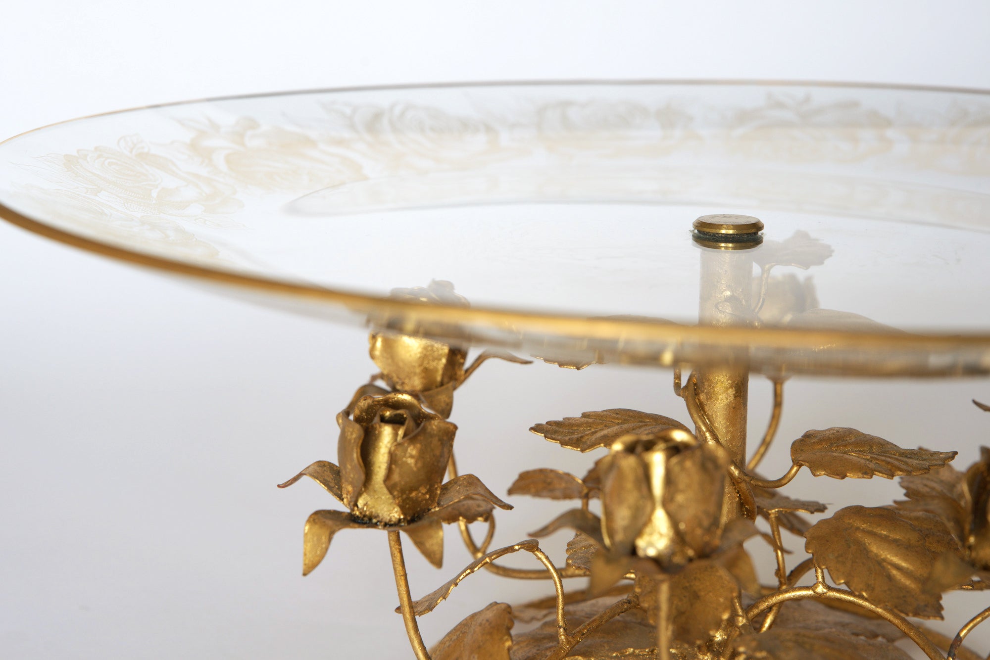 The Euro Trash Vintage Glass and Gilt Metal Rose Pedestal Cake Stand features ornate etched glass with a gold edge, resting on a decorative gilt metal base adorned with detailed roses and leaves.