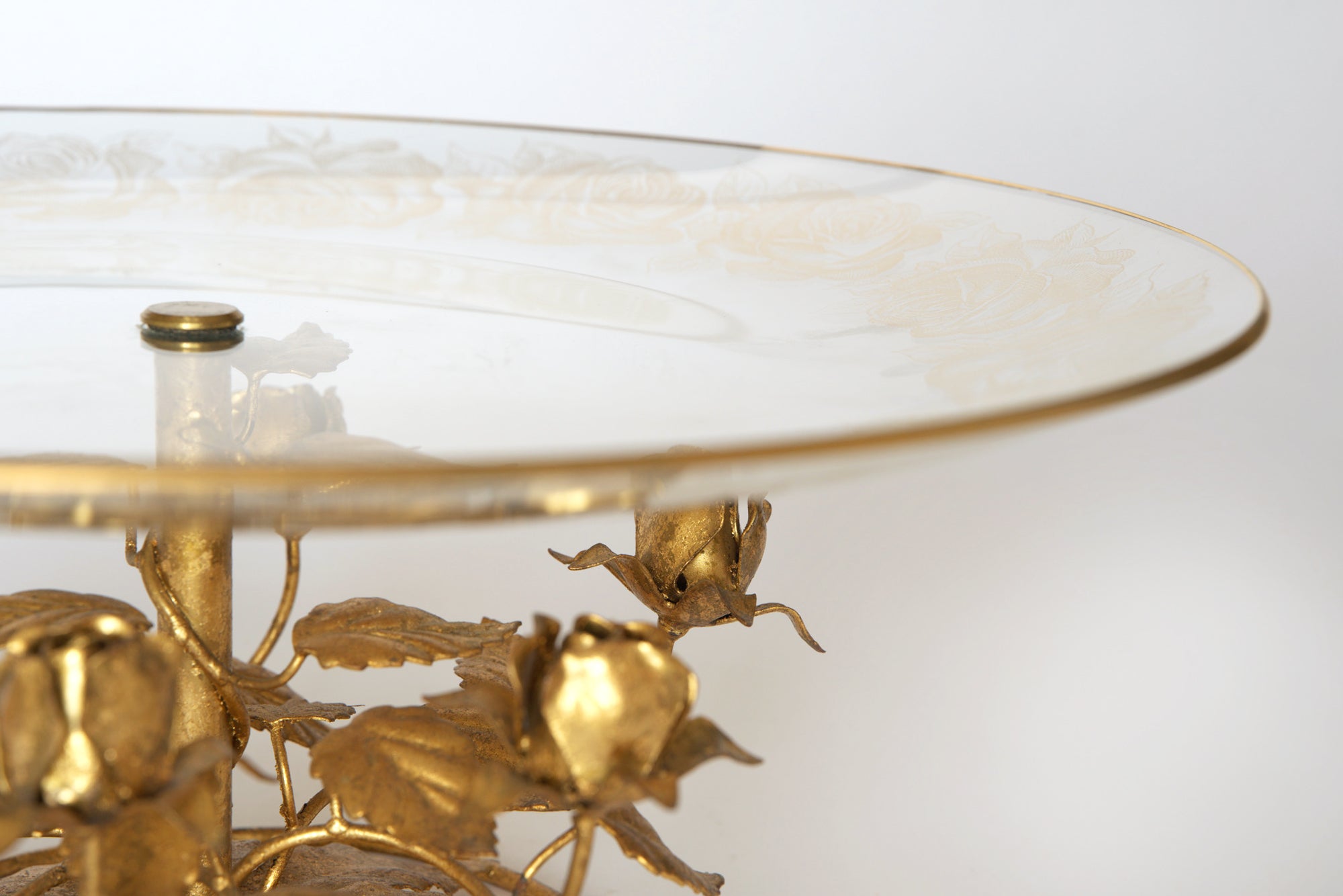 A close-up of the Euro Trash Vintage Glass and Gilt Metal Rose Pedestal Cake Stand, featuring decorative etched glass with floral designs atop an ornate gilt metal base adorned with detailed roses and leaves. Background is plain white.