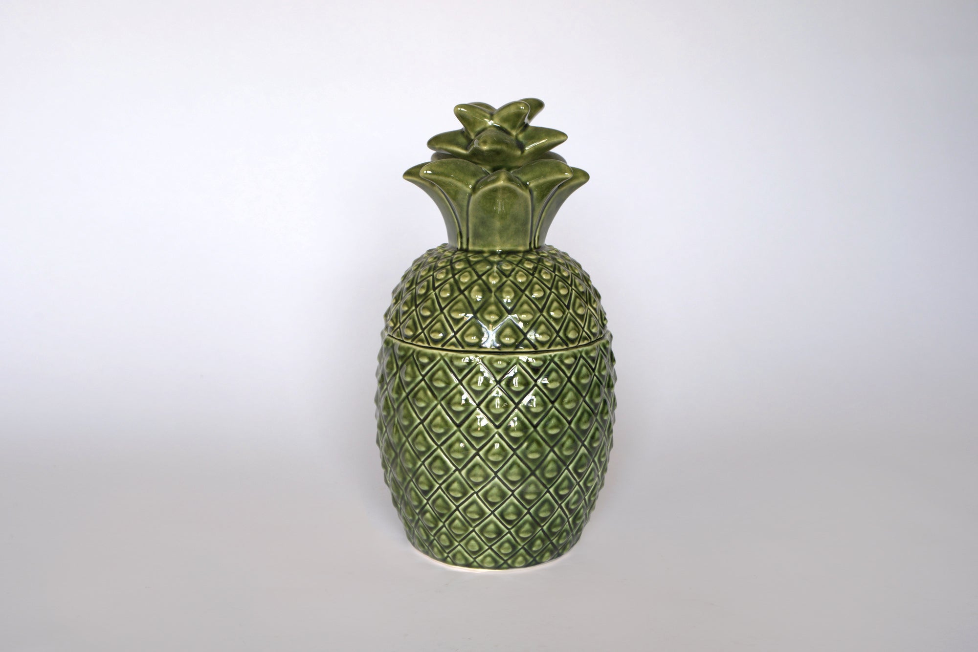 The Euro Trash Vintage Green Ceramic Pineapple Lidded Canister features a textured surface and removable top, ideal as a decorative storage jar or accent for tropical kitchen decor, shown on a plain white background.