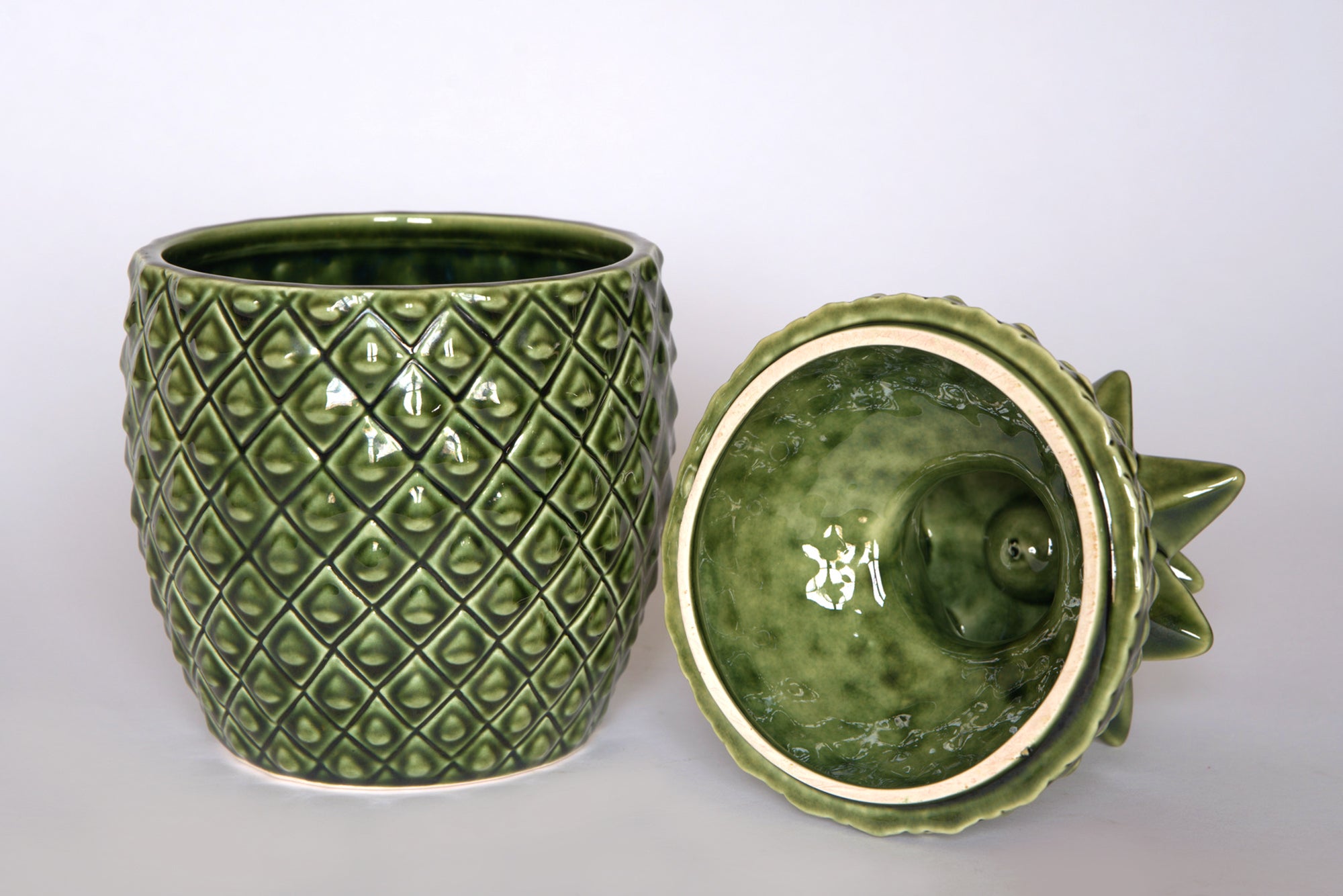 The Euro Trash Vintage Green Ceramic Pineapple Lidded Canister features a textured diamond design and serves as a stylish decorative storage jar, perfect for tropical kitchen decor. The upright canister pairs with its lid, shown resting to reveal the inside.