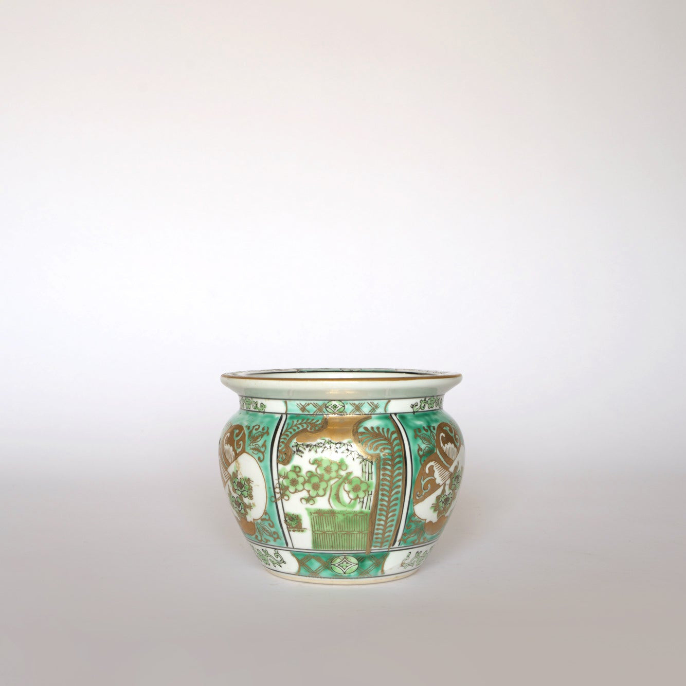 The Euro Trash Vintage Green and Gold Asian Motif Porcelain Cachepot showcases floral and geometric designs inspired by Asia, with green and gold patterns on a white background.