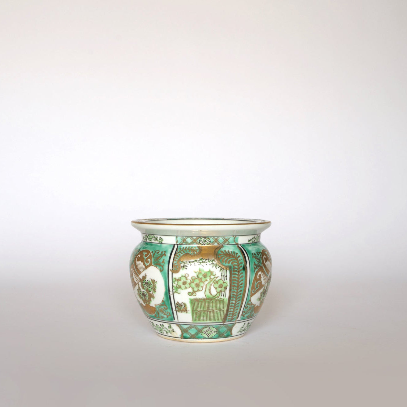 The Euro Trash Vintage Green and Gold Asian Motif Porcelain Cachepot features a rounded shape and decorative patterns of flowers, plants, and Asian-inspired motifs in green, brown, and white on a plain porcelain finish.