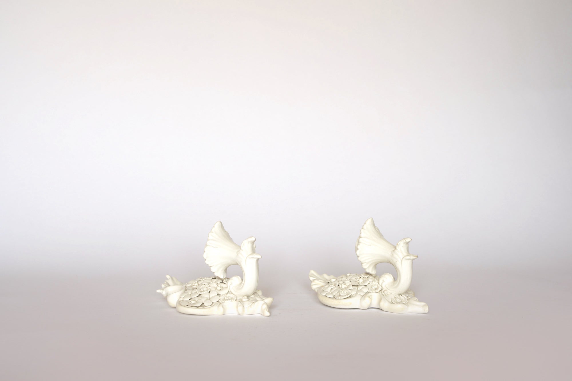 A pair of Euro Trash Porcelain Floral Wall Pocket Vases are displayed side by side on a light background, featuring detailed feathers and a classic style with raised wings; the swans face slightly toward each other.