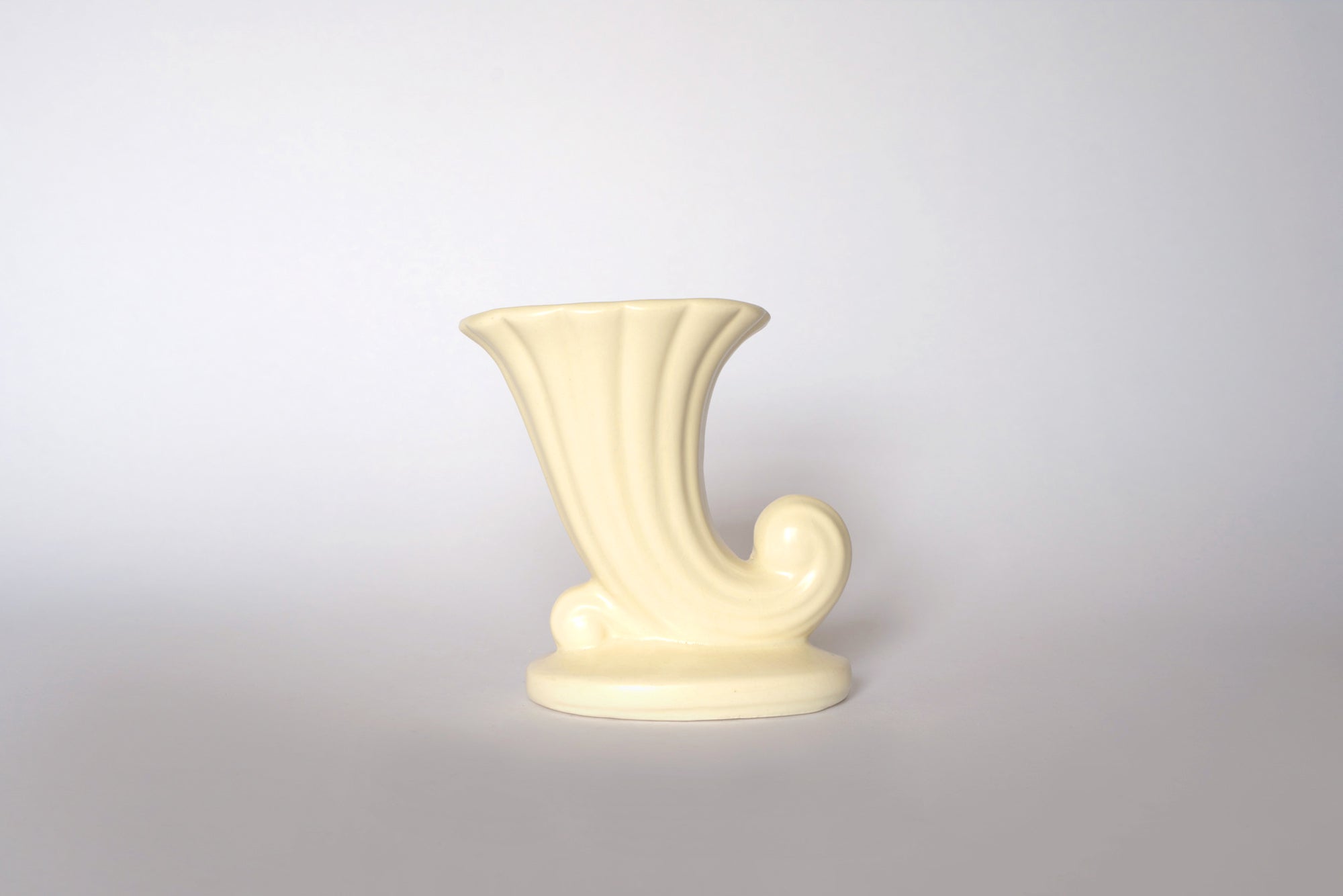The Euro Trash Vintage Cream Ceramic Cornucopia Vase features a swirled, fluted design, ideal for cottage-style decor and shown against a light gray background.