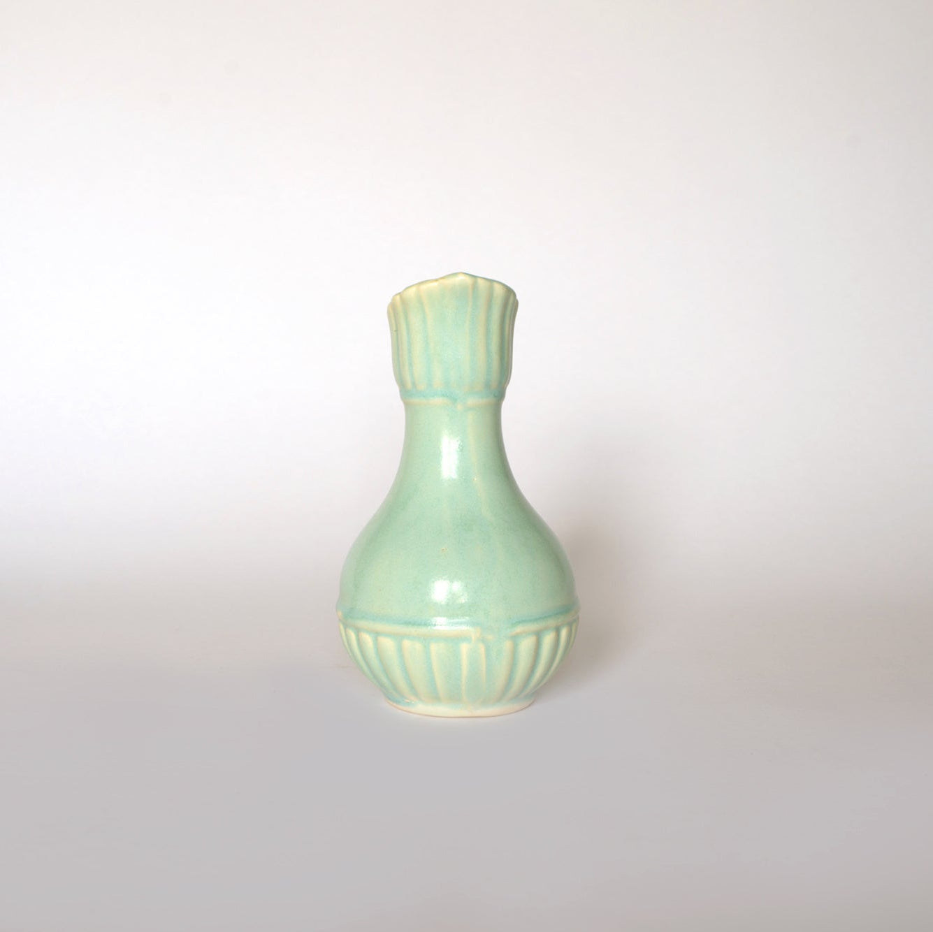 The Euro Trash Vintage Glazed Ceramic Pitcher Vase is a small, light green ceramic vase with a narrow neck, flared rim, and ribbed vertical accents on the top and bottom, shown against a plain white background.