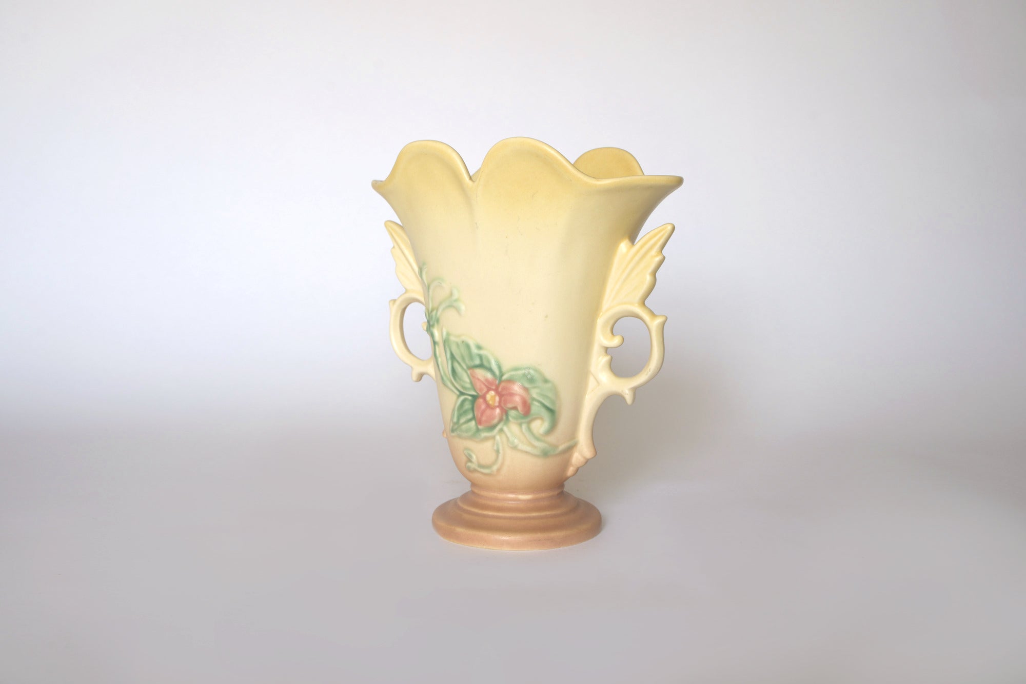 The Vintage Hull Floral Vase by Euro Trash features a pastel yellow finish, raised pink flowers with green leaves, scalloped rim, and two ornate handles—classic mid-century style—shown against a plain background.