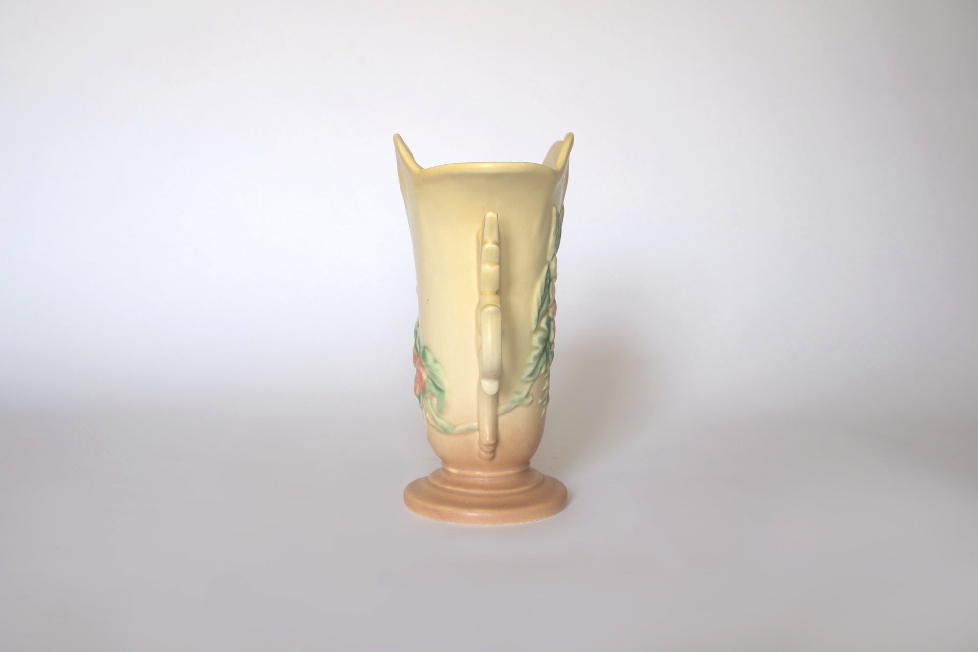 The Euro Trash Vintage Hull Floral Vase features a narrow neck, pastel yellow top, light brown base, and subtle raised floral patterns, all set against a plain white background.