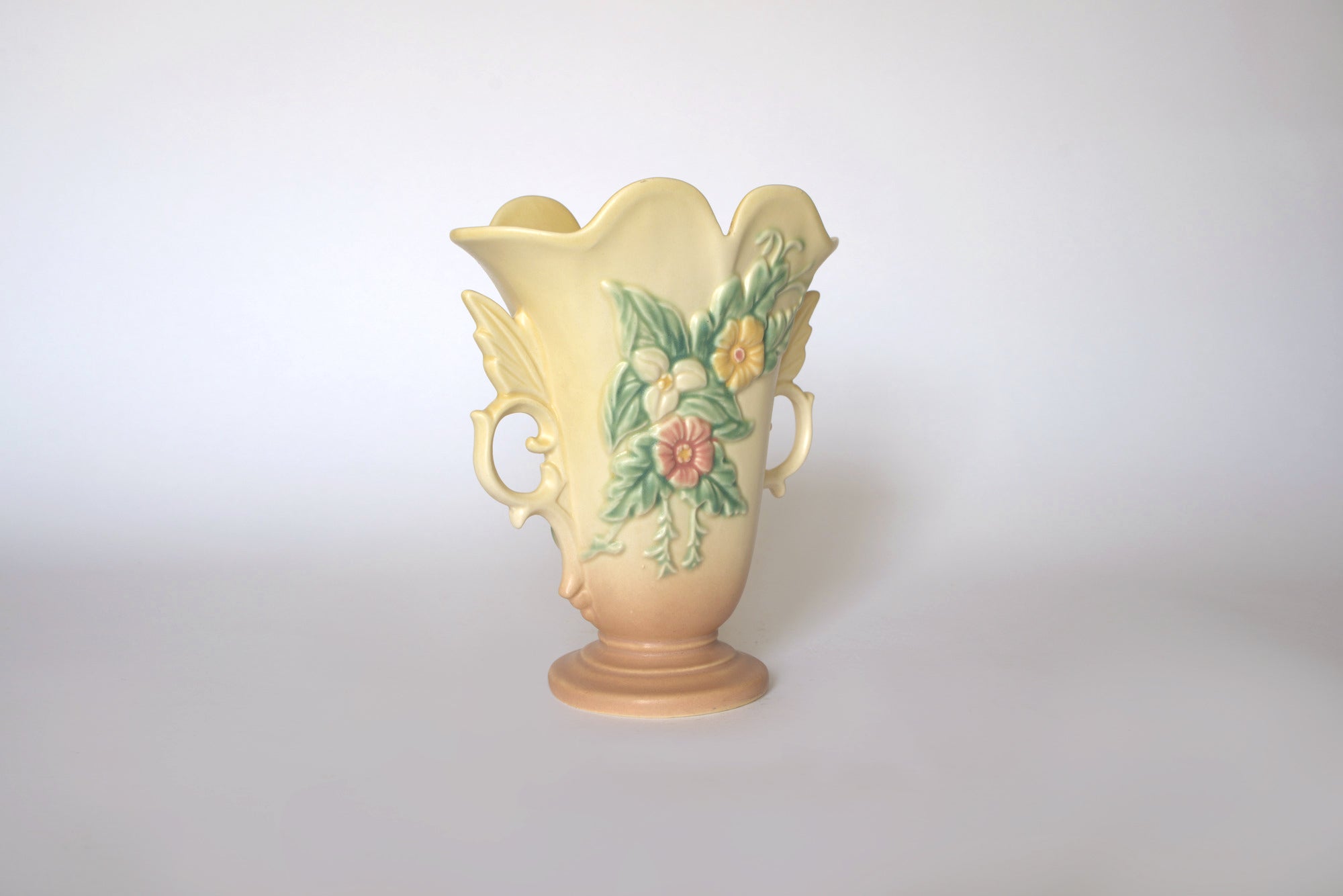 The Vintage Hull Floral Vase by Euro Trash features two handles and raised floral and leaf designs in pastel hues on a plain light background.