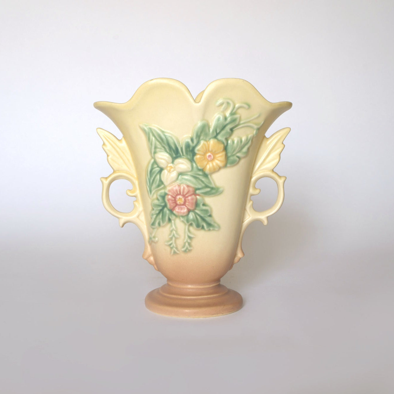 The Vintage Hull Floral Vase by Euro Trash features scalloped edges, ornate handles, and raised pastel floral designs in yellow, green, and pink on a ceramic base, capturing classic Hull Pottery style against a simple light background.