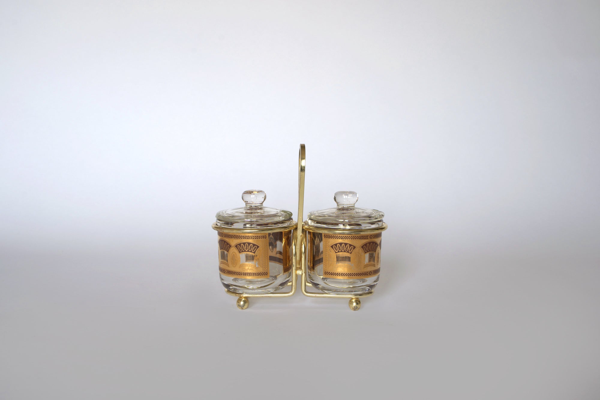 The Euro Trash Vintage Gold Caddy Double Glass Jar Set features two glass jars with gold labels and lids in a sleek gold caddy, adding mid-century flair to your kitchen decor against a clean white background.