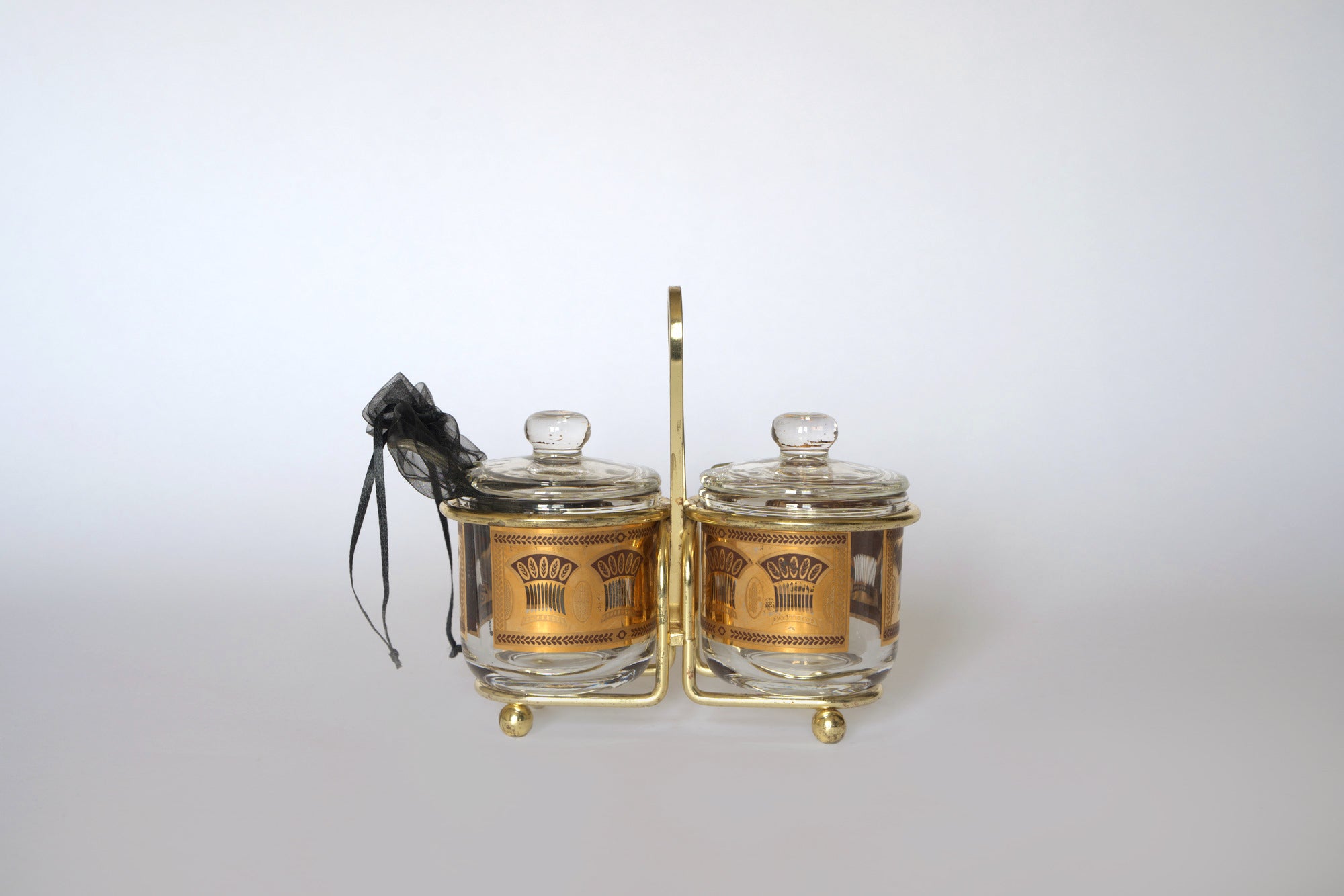 The Euro Trash Vintage Gold Caddy Double Glass Jar Set features two clear jars with gold lids in a decorative metal caddy, plus a black drawstring bag—ideal for adding mid-century charm to your kitchen decor.
