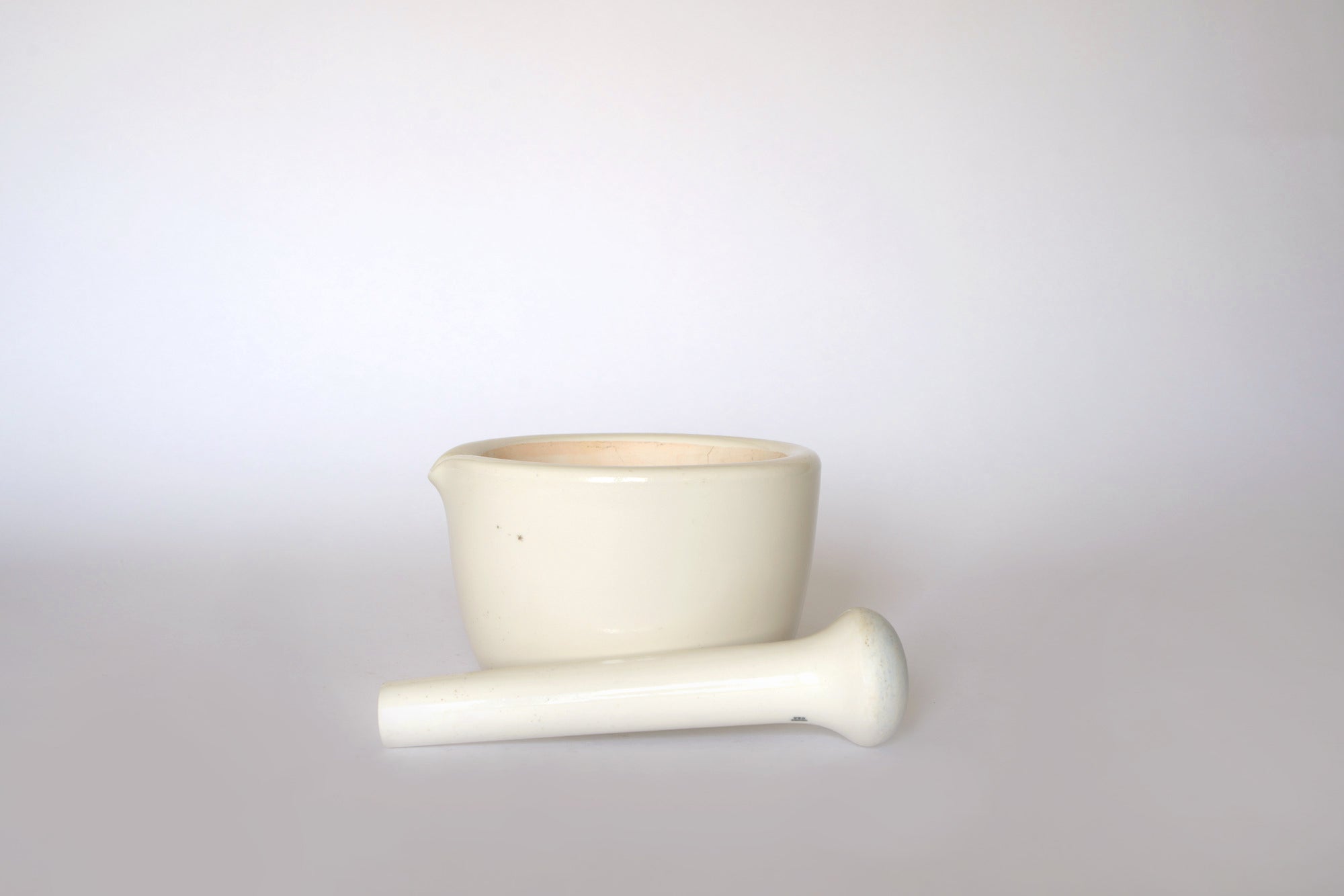 The Euro Trash Vintage White Ceramic Mortar and Pestle Set sits on a plain light background with the pestle in front—ideal as stylish kitchen decor or for everyday culinary tasks.