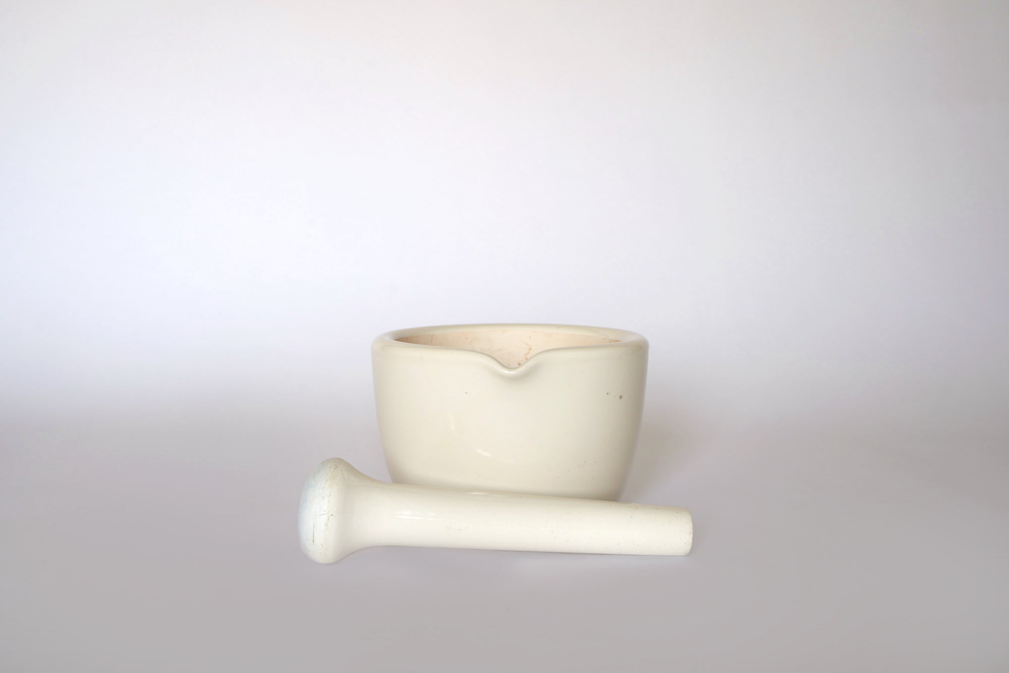 The Euro Trash Vintage White Ceramic Mortar and Pestle Set is shown upright on a light background, with the pestle in front—an elegant decorative kitchen accessory.