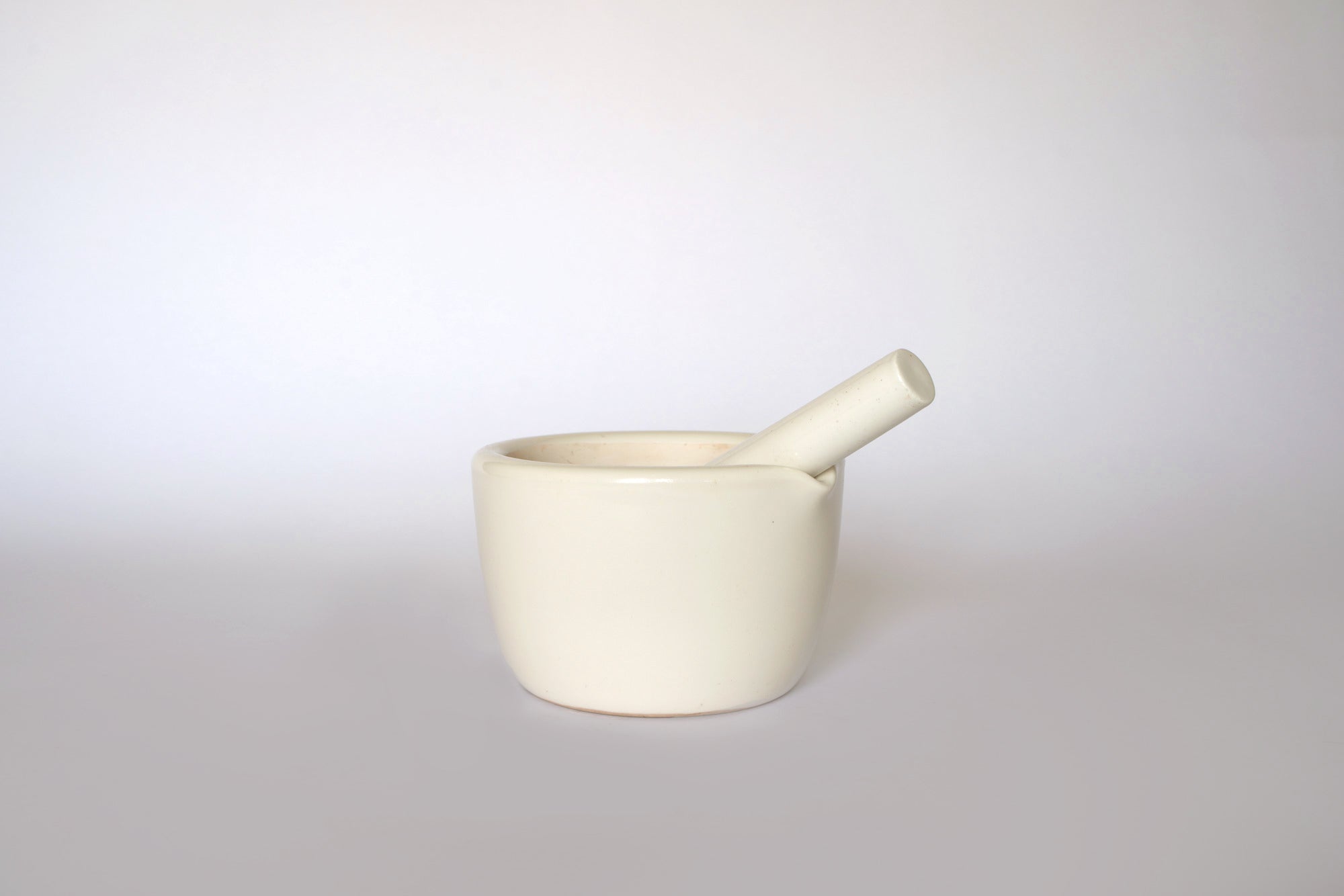 The Euro Trash Vintage White Ceramic Mortar and Pestle Set sits on a light surface with a white background, making it an ideal decorative kitchenware piece.