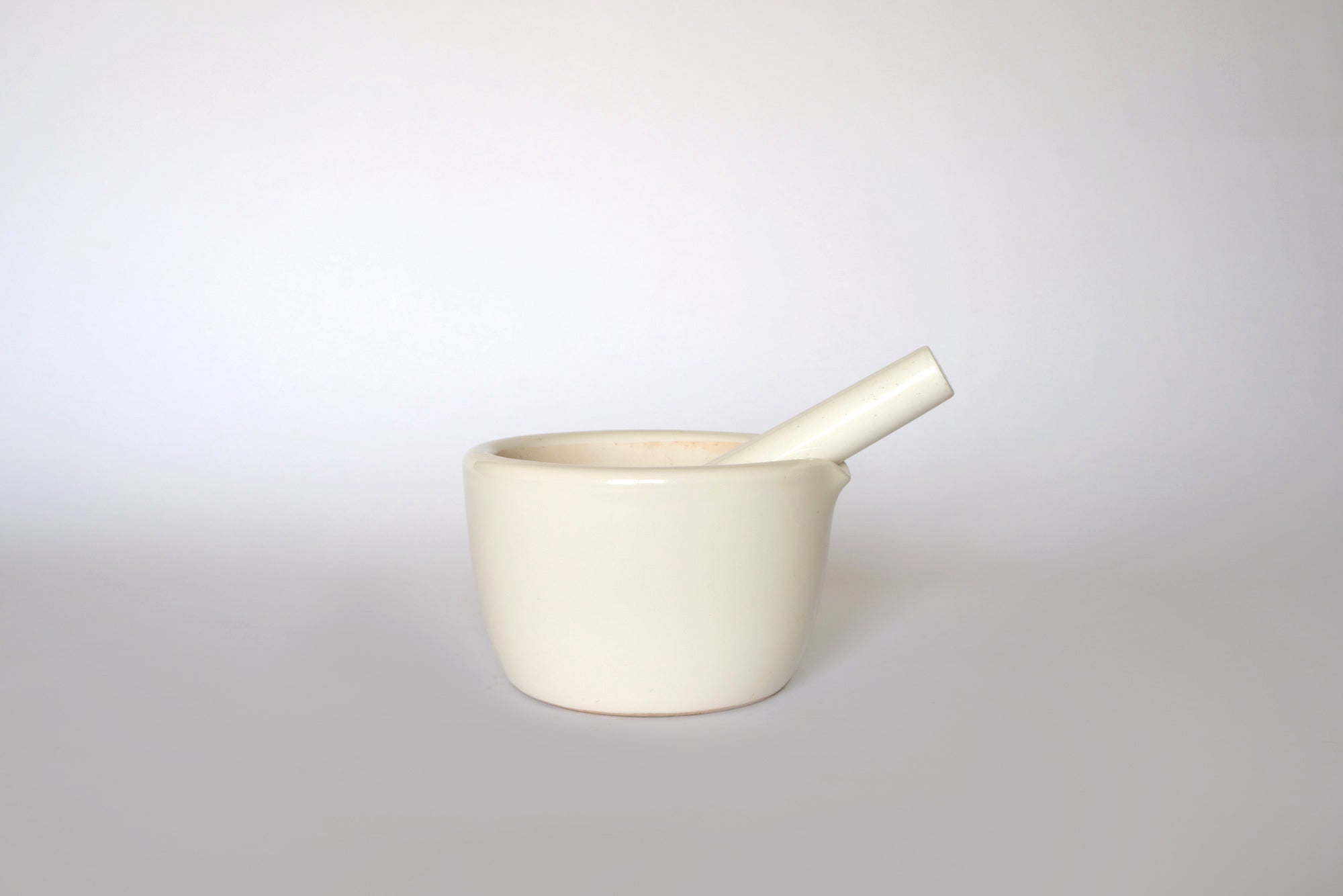 The Euro Trash Vintage White Ceramic Mortar and Pestle Set, a classic decorative kitchenware piece, sits centered on a plain, light background.
