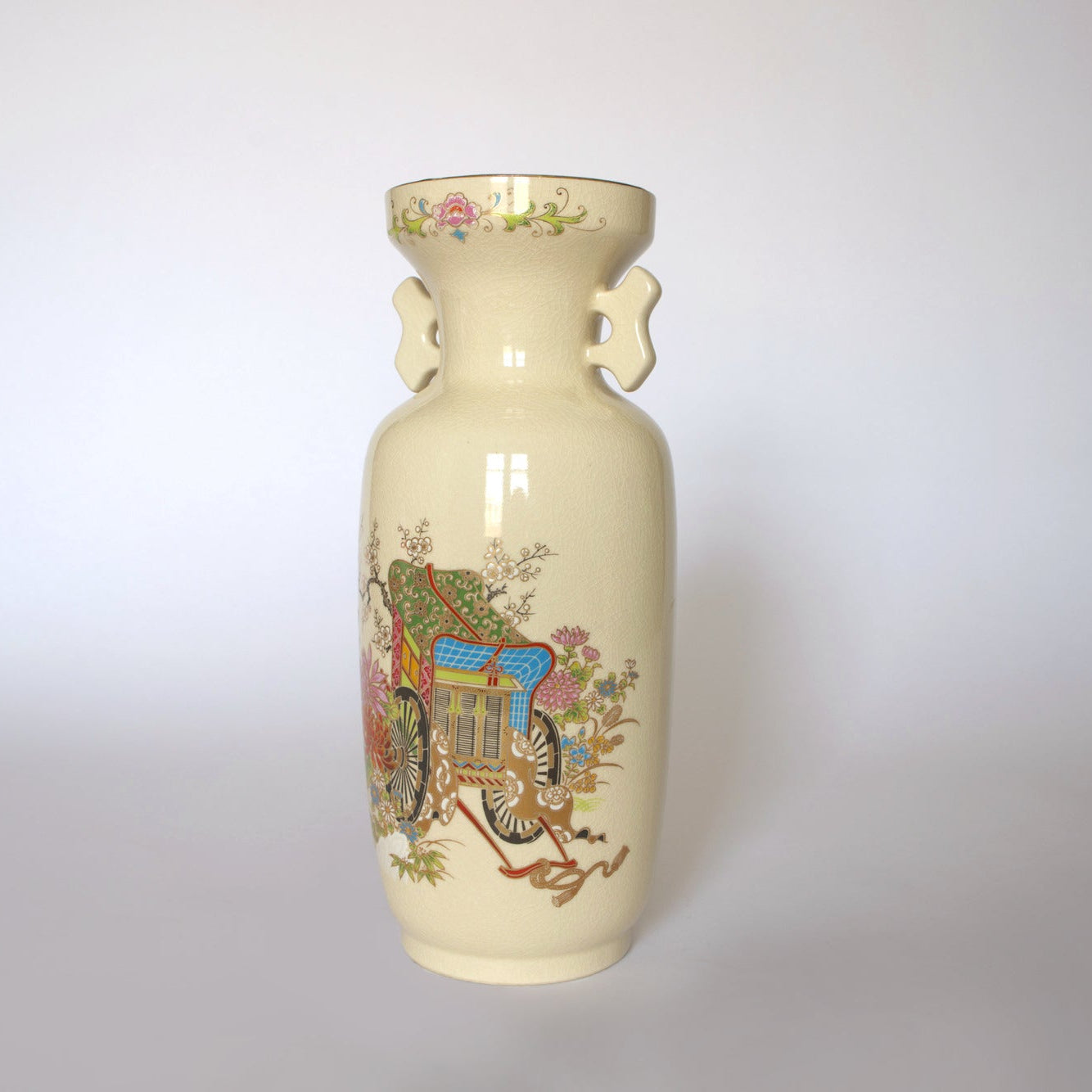 The Euro Trash Vintage Japanese Satsuma Style Ceramic Vase is a tall, cream-colored piece with handles, adorned with a colorful painted Asian carriage and floral design—an elegant decorative statement.