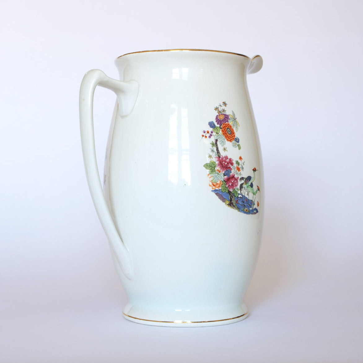 The Euro Trash Vintage Floral Porcelain Pitcher features a curved handle, vibrant floral pattern, and gold-trimmed rim, displayed on a plain white background.