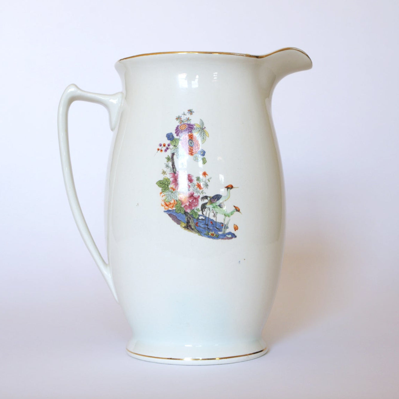The Euro Trash Vintage Floral Porcelain Pitcher features a curved handle, vibrant floral design, and elegant crane motifs on one side, set against a plain light background.