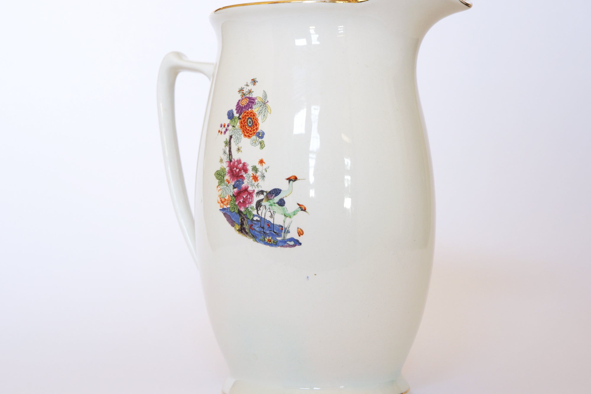 The Euro Trash Vintage Floral Porcelain Pitcher features a handle, colorful floral and bird motifs, a gold-accented rim, and a plain white background.