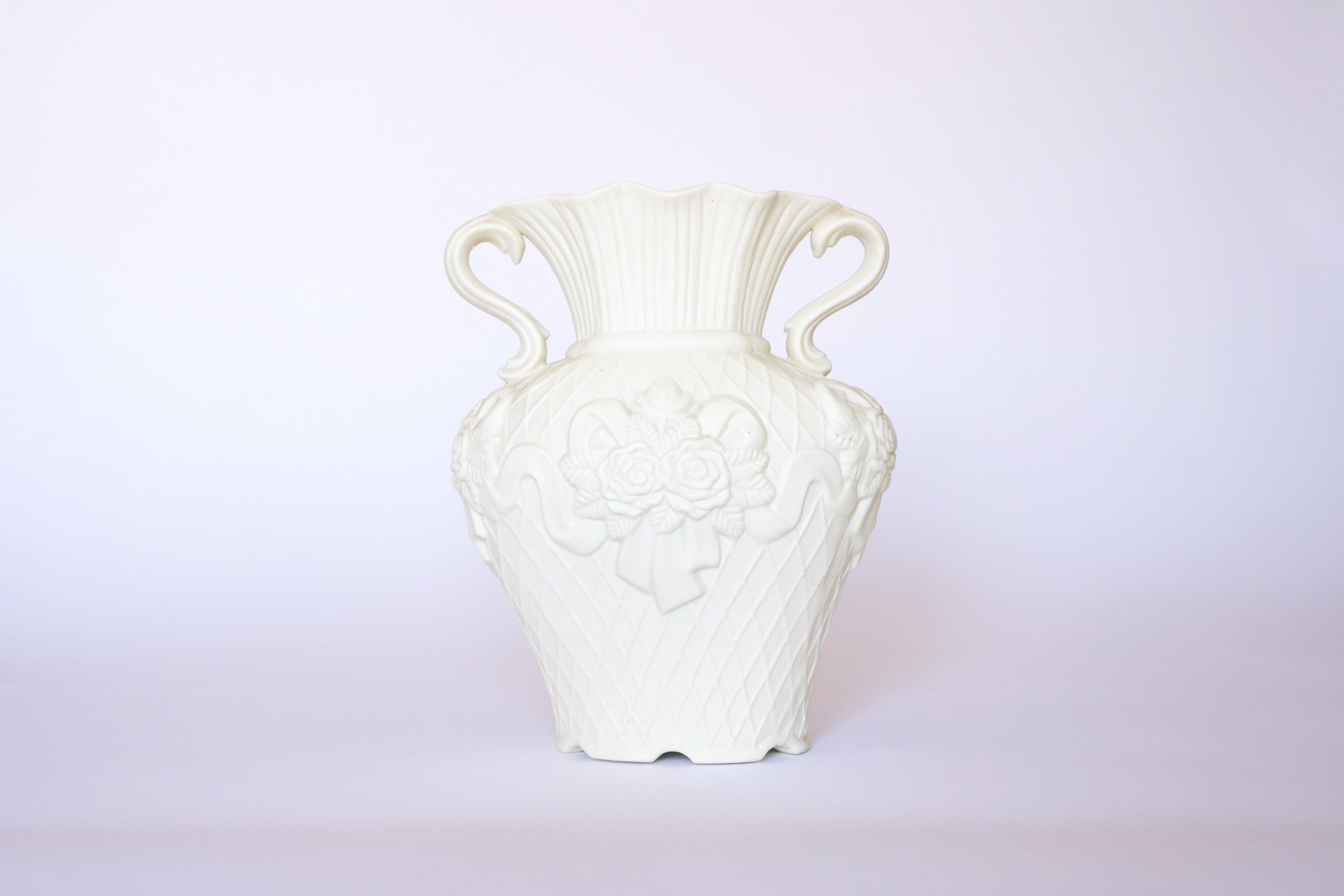 The Euro Trash Annie Vintage White Ceramic Relief Floral Vase features ornate handles and embossed flowers with ribbon designs, making it a perfect piece of ornamental decor against any light background.