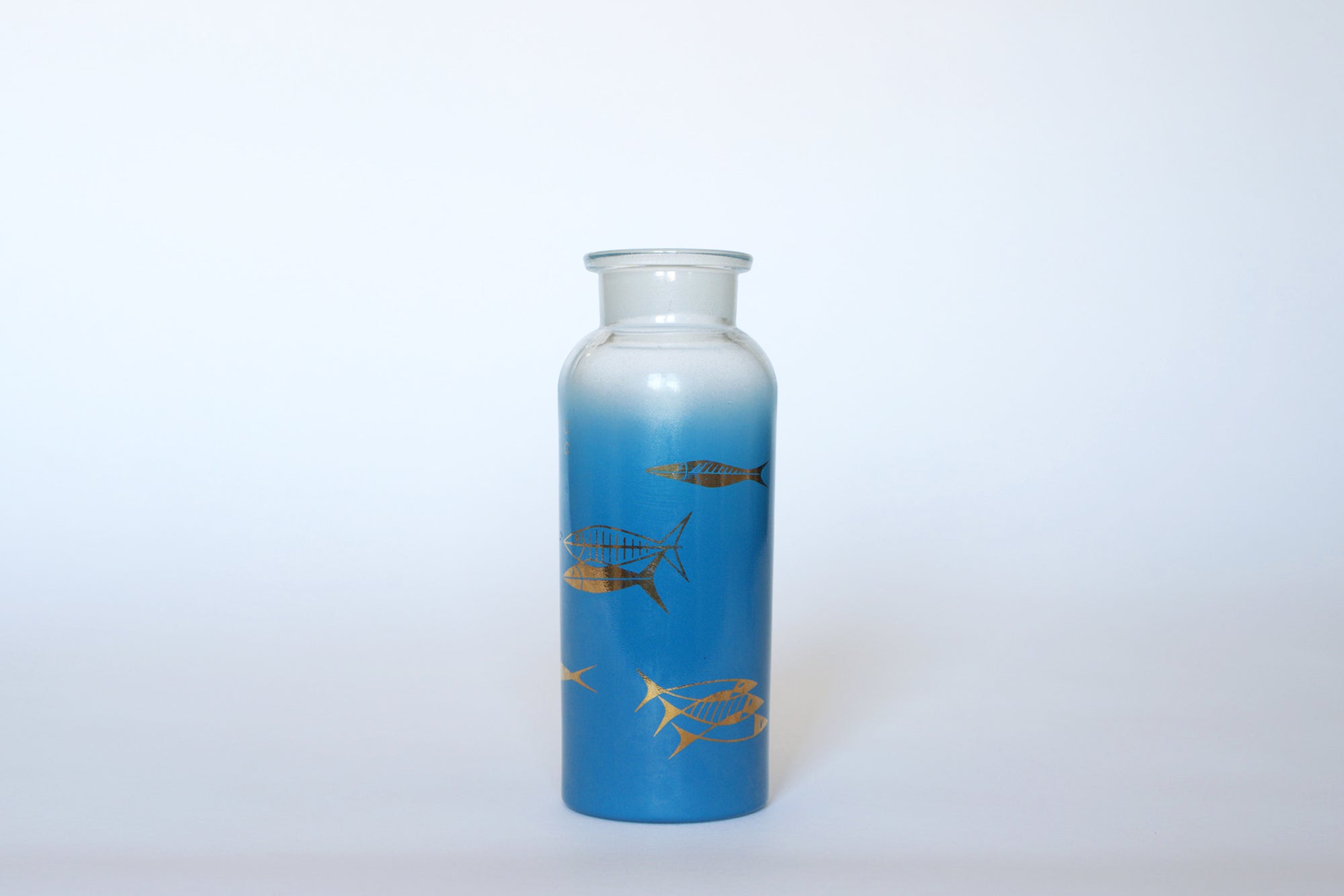 The Euro Trash Vintage Blue Frosted Glass Vase features a tall, cylindrical shape with a blue gradient and gold and black fish illustrations, displayed against a plain white background.
