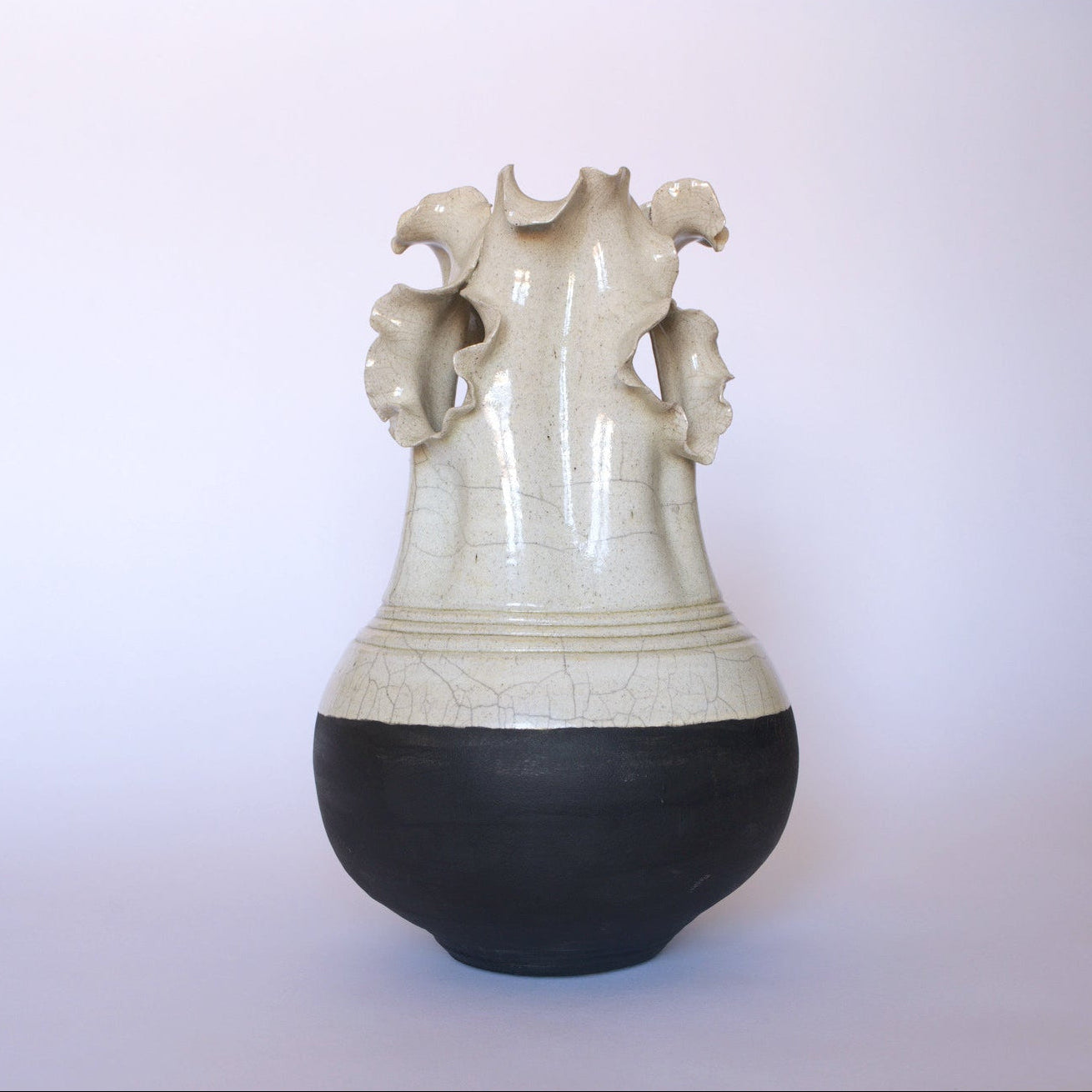 The Euro Trash Vintage Two-Tone Glaze Vase with Ruffled Rim features a round black base, glossy beige upper section, and a sculptural flared neck with petal-like edges, highlighted against a plain light background.