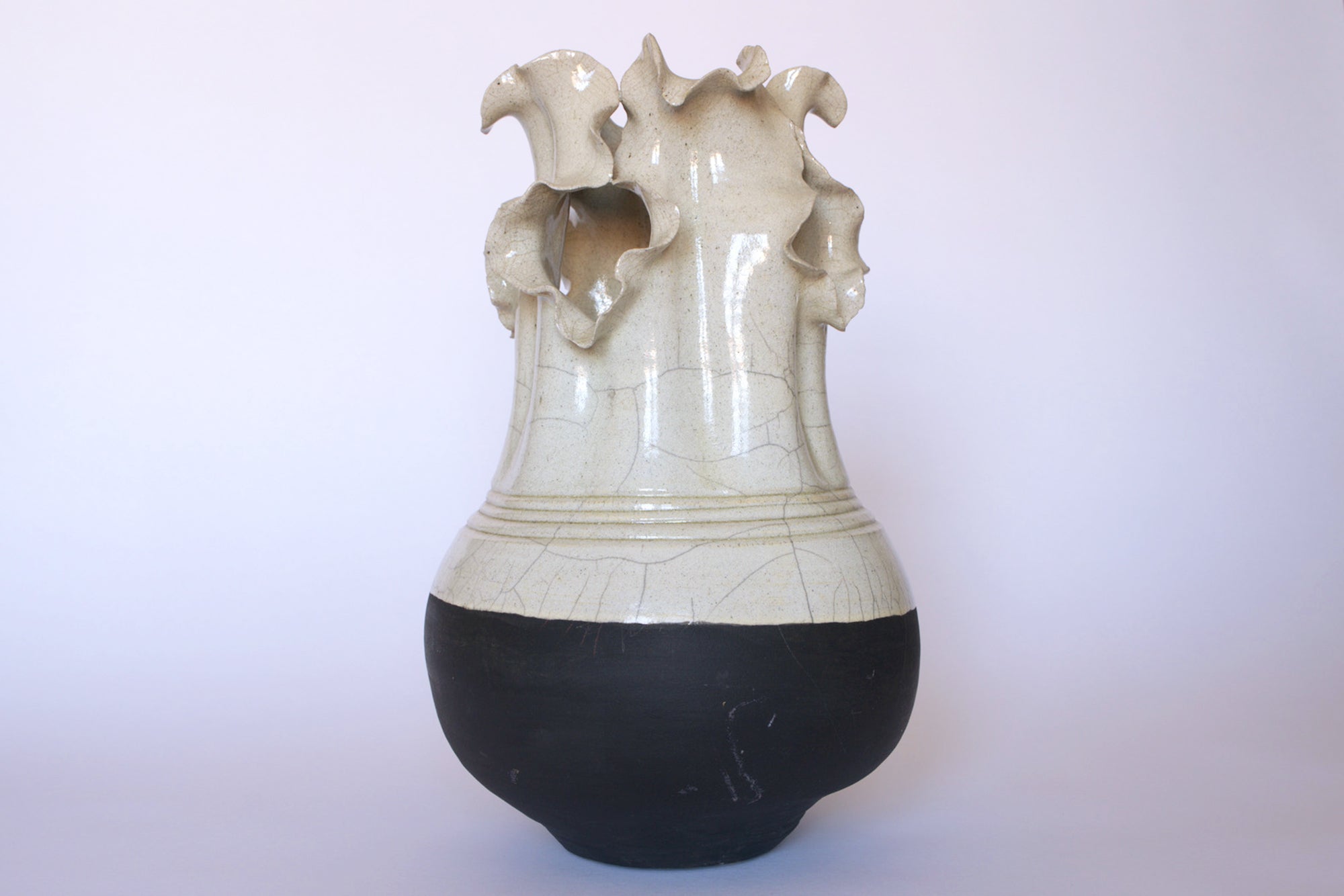 The Vintage Two-Tone Glaze Vase with Ruffled Rim by Euro Trash features a rounded black base, cream upper body, abstract wavy rim, and textured crackle glaze lines for a rustic studio pottery look.