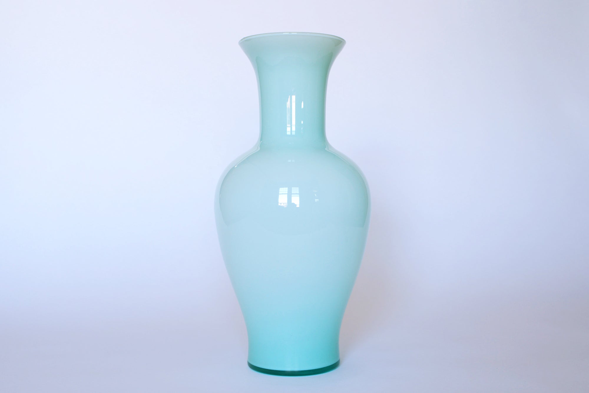 The Euro Trash Vintage Pale Blue Glass Vase features a tall, glossy, minimalist design with a narrow neck and wide base, showcased against a plain white background.